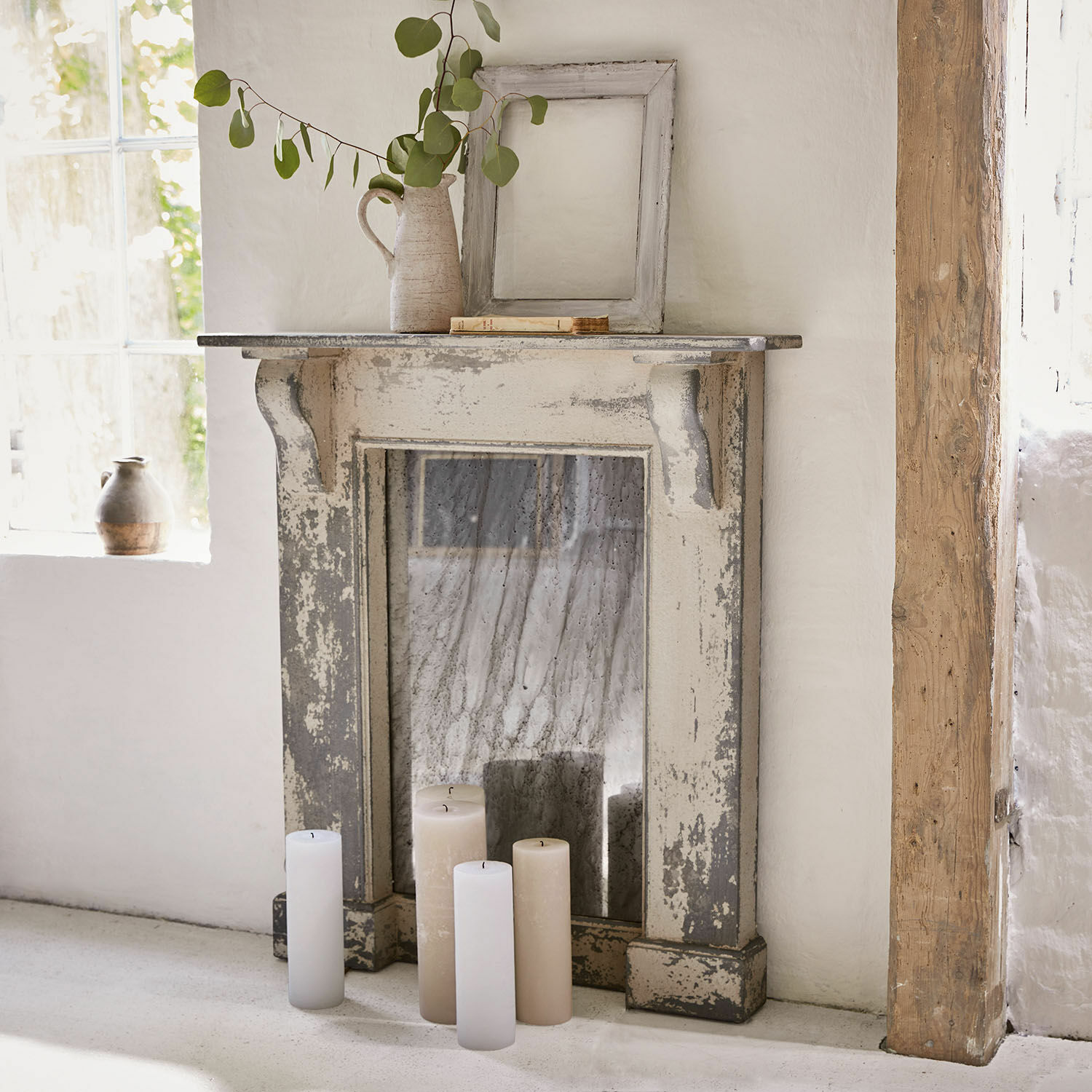 Rustikaler Dekokamin aus gealtertem Holz in Grau-Beige mit weißen Kerzen für gemütliche Atmosphäre