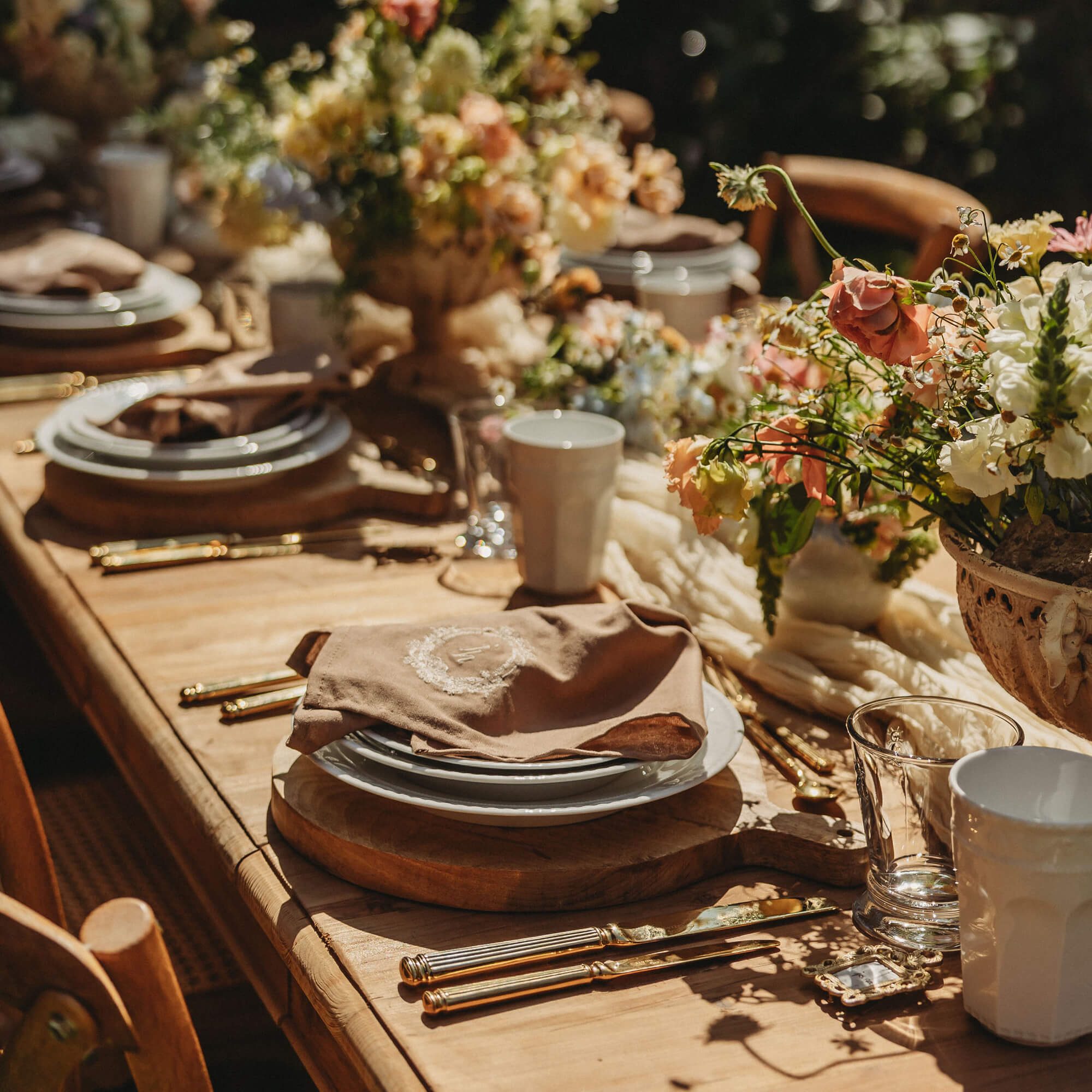 Rustikaler Holztisch mit Geschirr, goldenen Bestecken und Blumenarrangement für festliches Essen