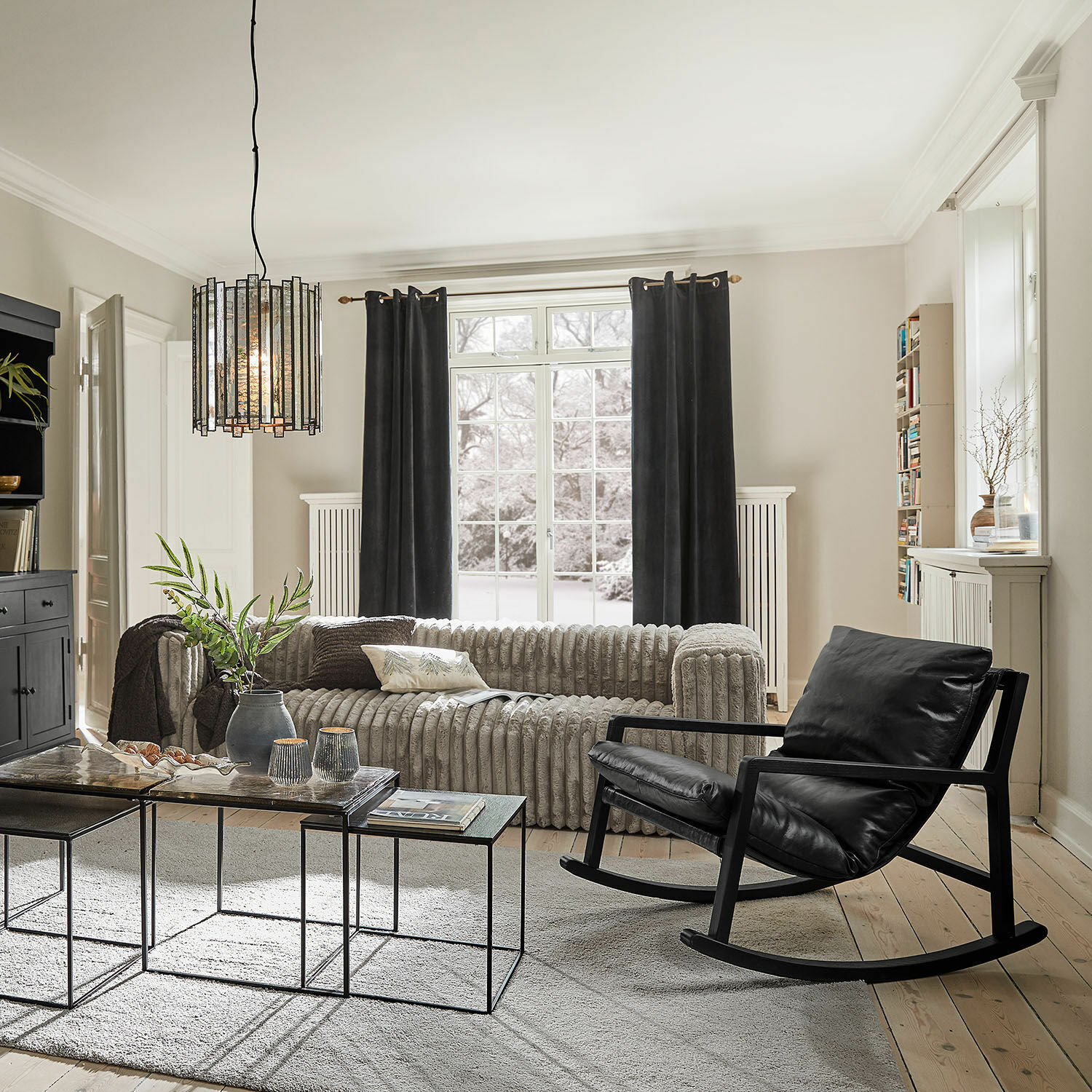 Modernes Wohnzimmer mit schwarzem Leder-Schaukelstuhl und grauem Stoffsofa, Metall-Glas-Couchtische