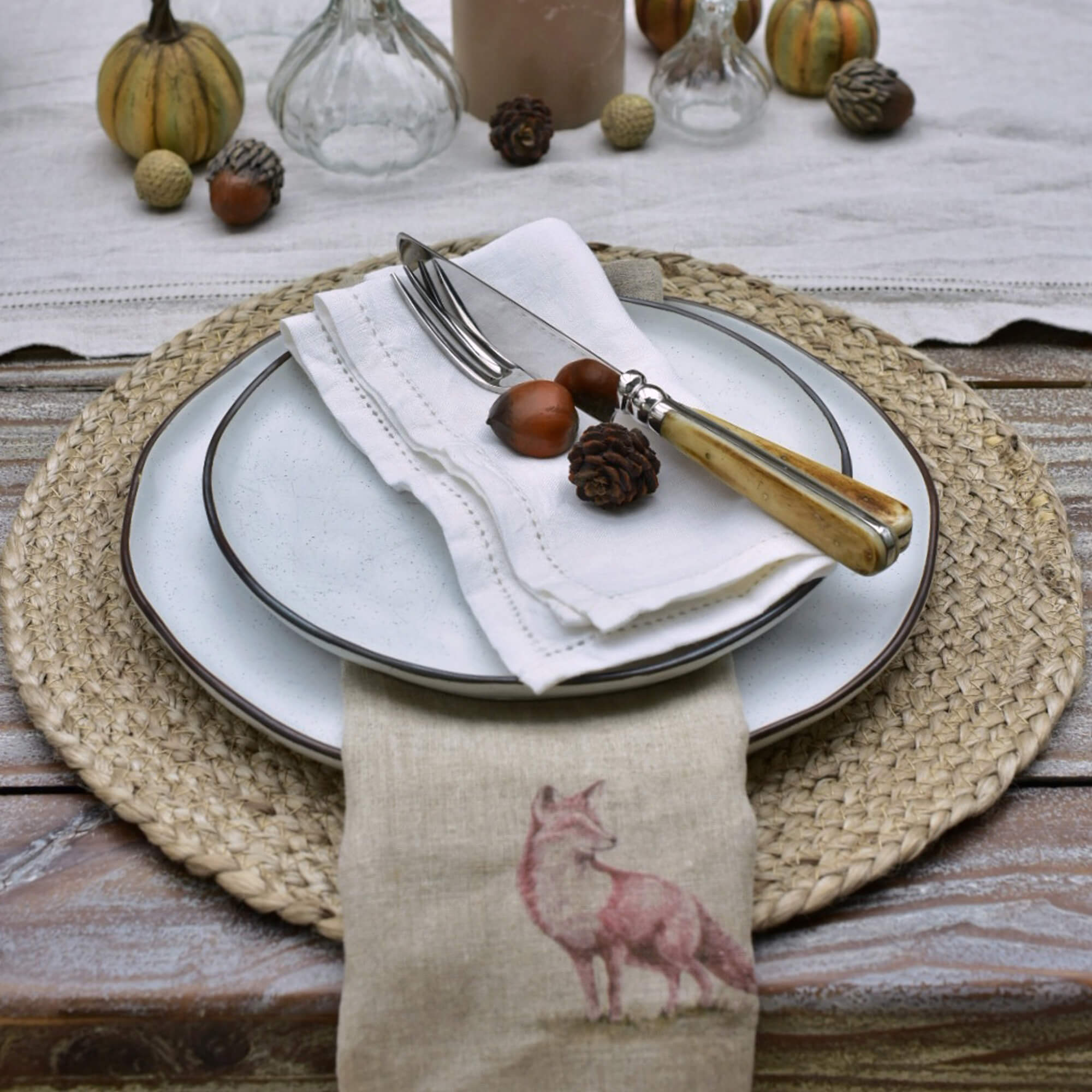 Tischgedeck mit weißen Keramiktellern, Besteck mit hellem Holzgriff und Leinenserviette mit Fuchsmotiv