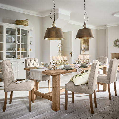 Esszimmer mit massivem Holztisch und beige gepolsterten Stühlen, zwei Metall-Hängeleuchten