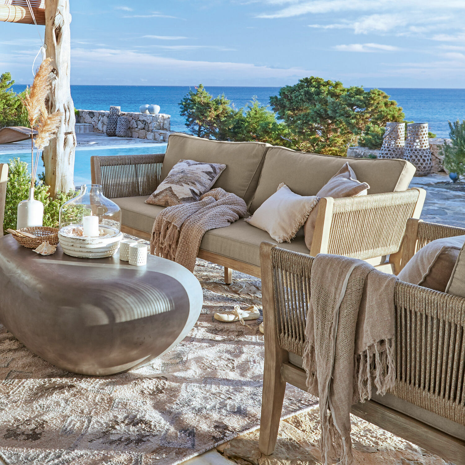 Outdoor-Möbelset mit beigen Polstern und grauem Steintisch auf Terrasse mit Meerblick