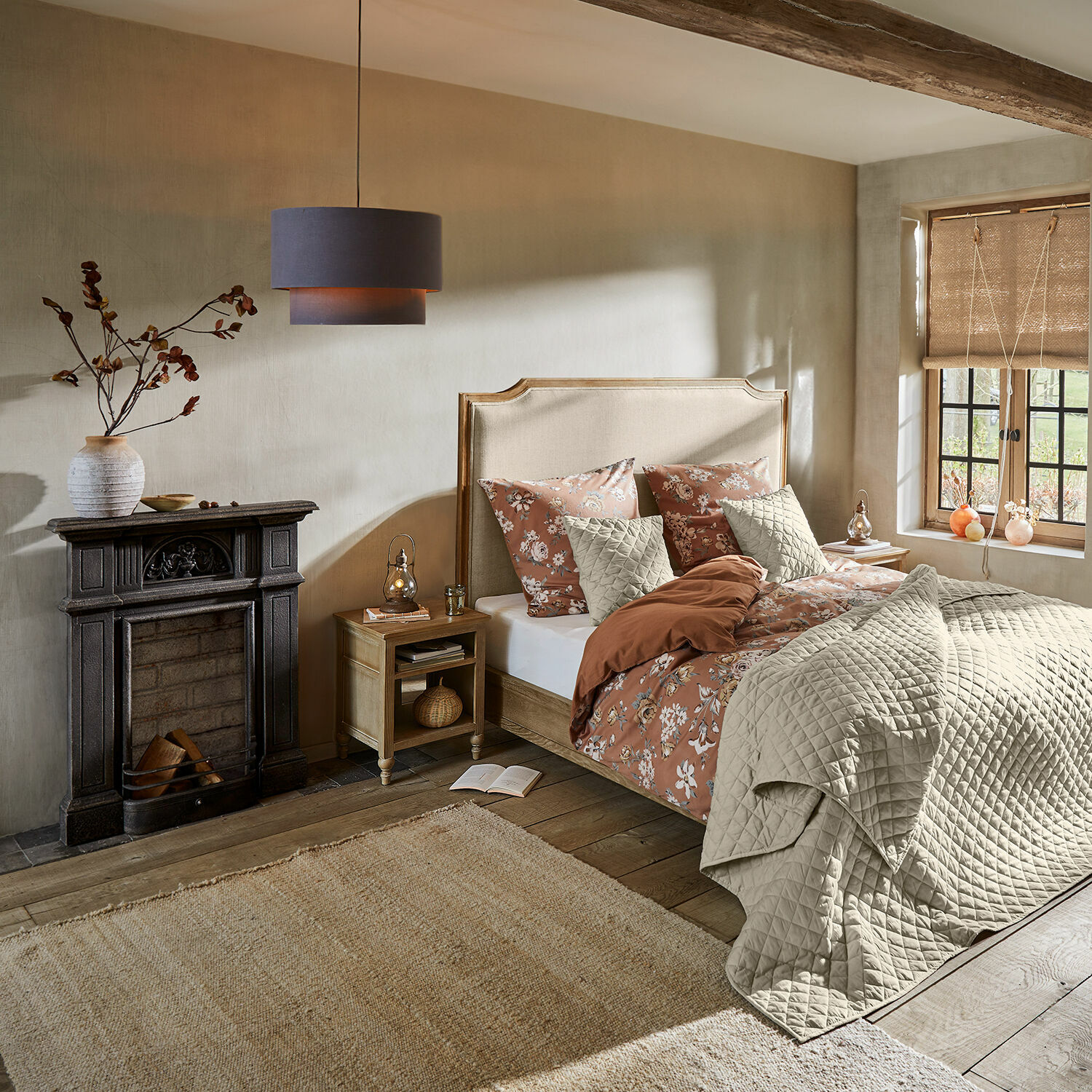 Gemütliches Schlafzimmer mit beige gepolstertem Kopfteil, floraler Bettwäsche in warmen Tönen und Naturteppich
