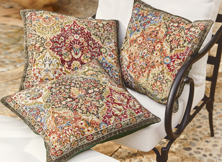 Drei dekorative Kissen mit orientalischem Muster in warmen Farben auf weißem Metallstuhl