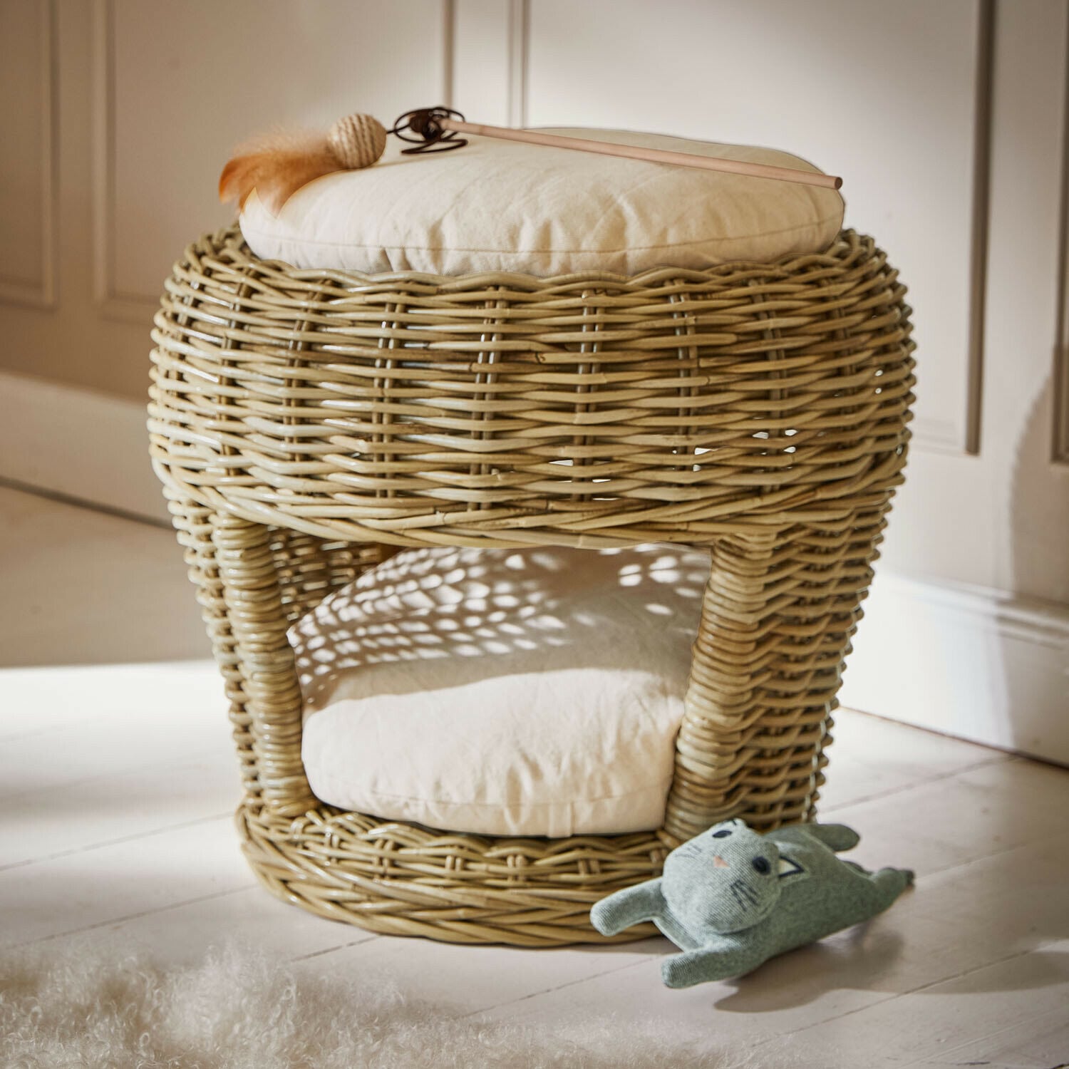 Runder Rattan-Hocker mit cremefarbenem Kissen und Katzenspielzeug auf dem Boden, natürliche Materialien