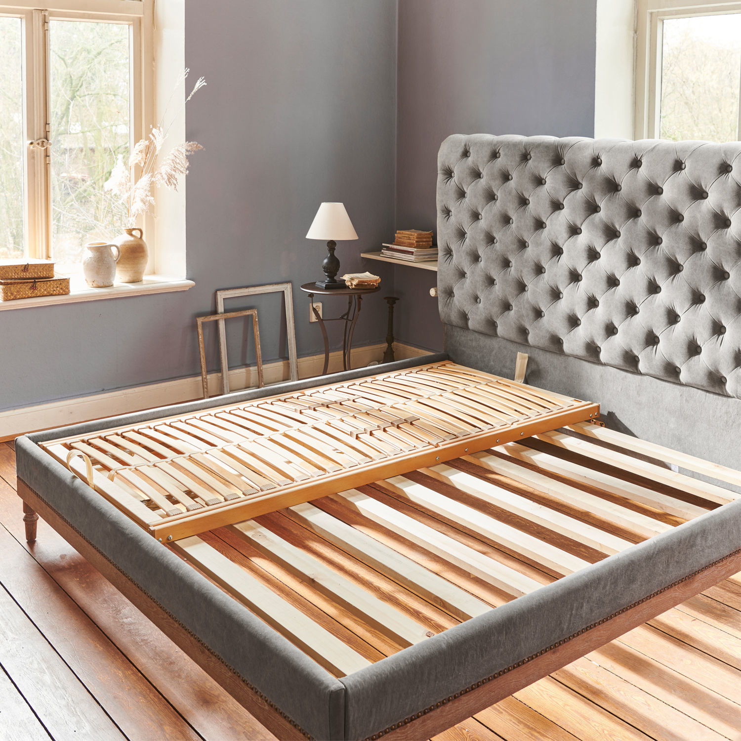 Grau bezogenes Bett mit gesteppter Kopfstütze und Holzrahmen in hellem Zimmer mit Holzboden