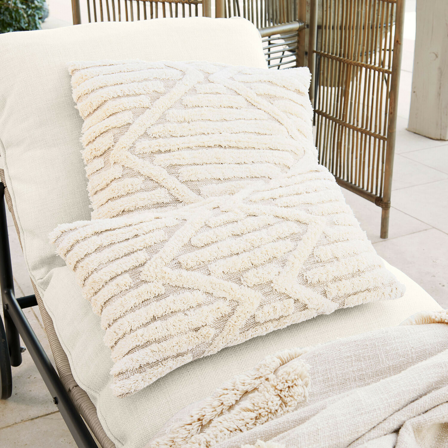 Zwei cremefarbene Dekokissen aus weichem Material mit geometrischem Muster auf hellem Liegestuhl