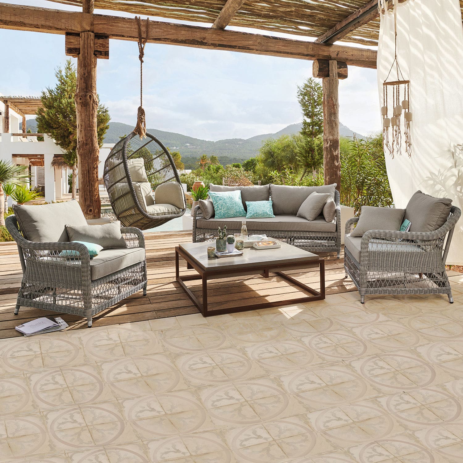 Sitzgruppe Tanaiste Gartenmöbel-Set aus grauem Rattan mit Polstern und hängendem Korbsessel auf Terrasse mit Bergblick