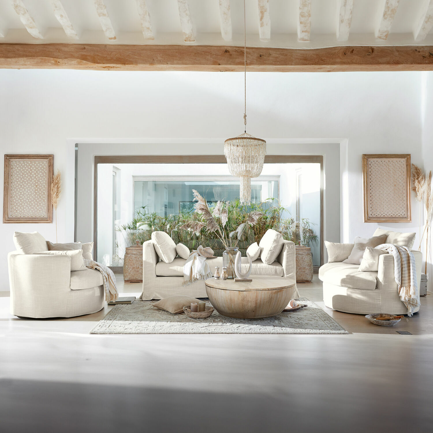 Helles Wohnzimmer mit beigen Polstersesseln und Sofa, rundem Holztisch und dekorativem Teppich