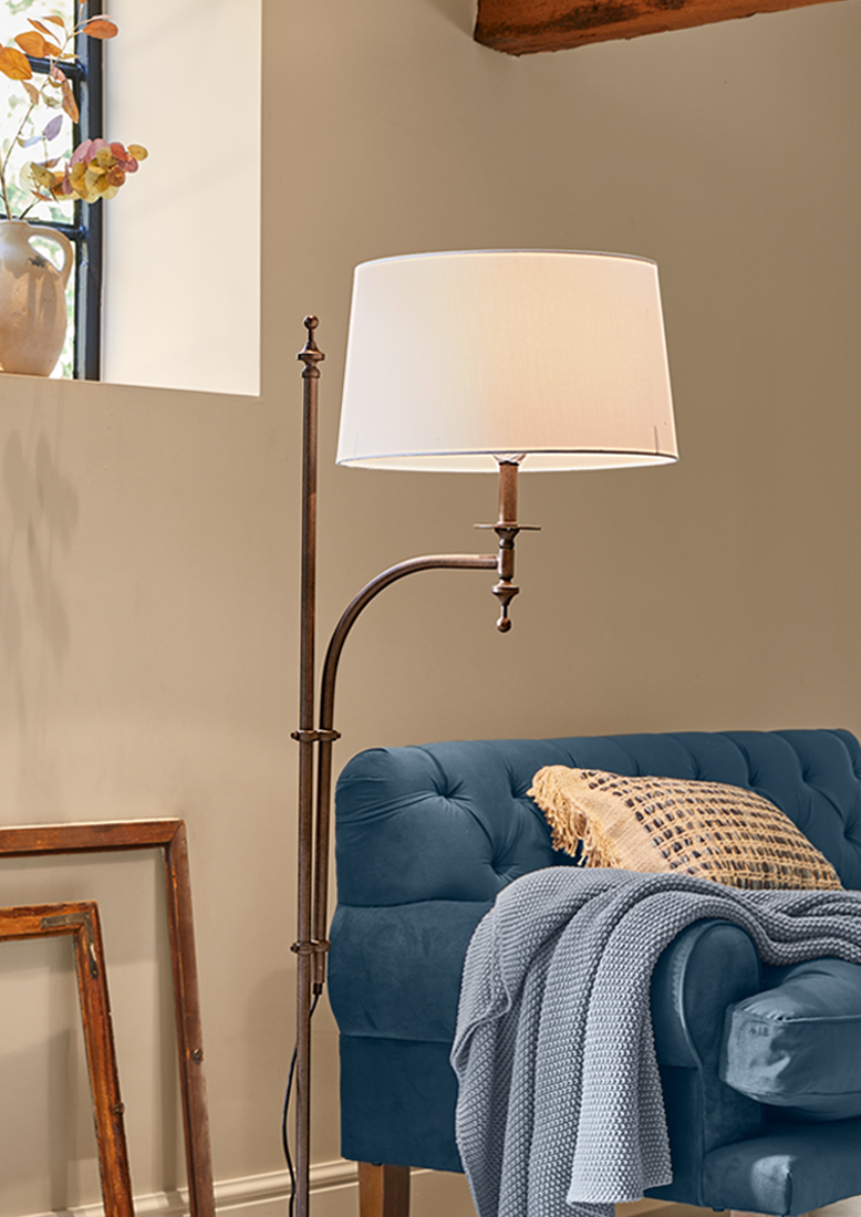 Stehlampe mit Metallgestell und weißem Lampenschirm neben blauem Sofa mit Strickdecke