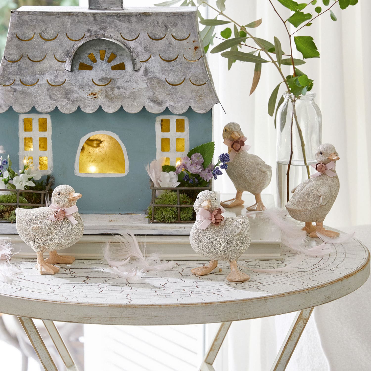 Küken 4er Set Orélie Dekorative Entenfiguren aus hellem Material auf weißem Tisch mit Haus und Blumenarrangement