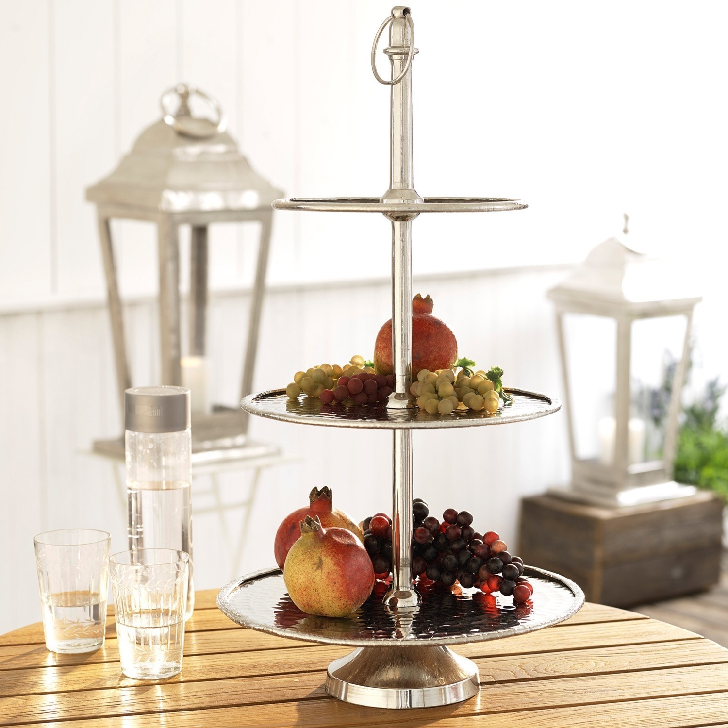 Zweistöckige Etagere aus Edelstahl mit Granatäpfeln und Trauben auf Holztisch