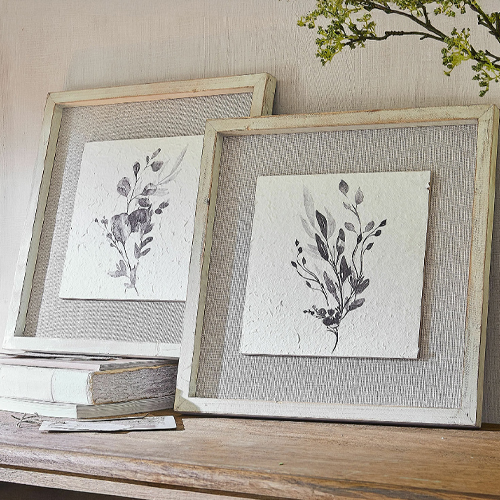 Zwei rustikale helle Holzrahmen mit pflanzlicher Grafik auf Netzstoff, Wanddekoration im Landhausstil