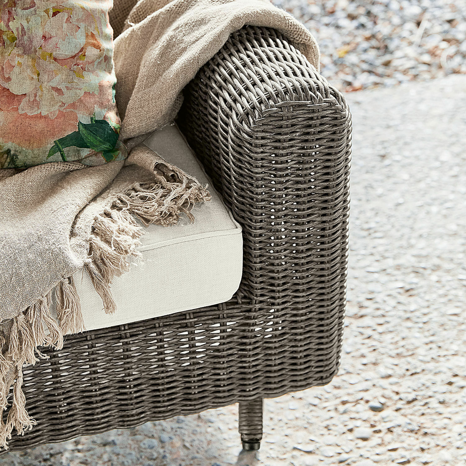 Ecksofa aus grauem Geflecht mit hellbeigem Polster und dekorativer beige Decke