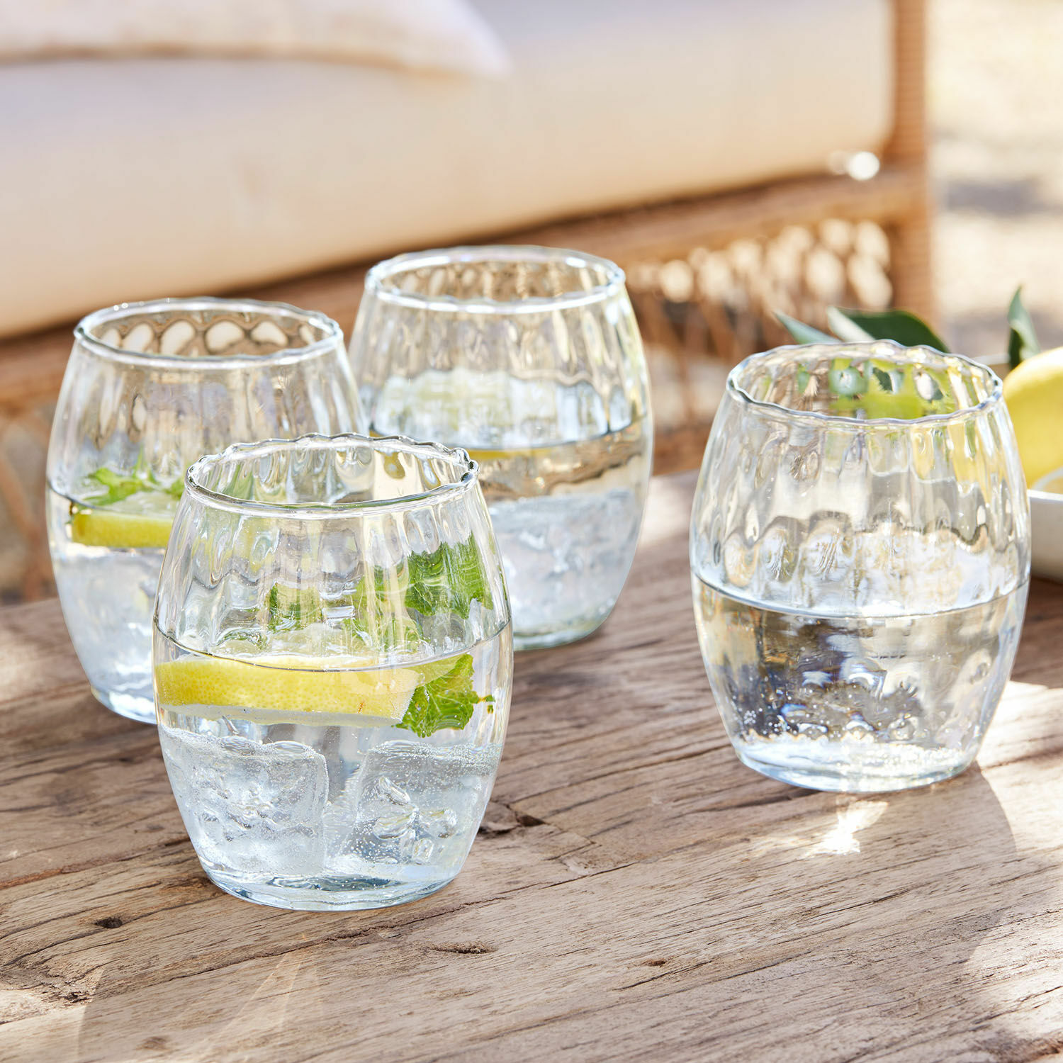 Glas 4er Set Bourgavin Vier Gläser aus klarem Glas mit Wasser, Eis und Zitrone auf einem Holztisch