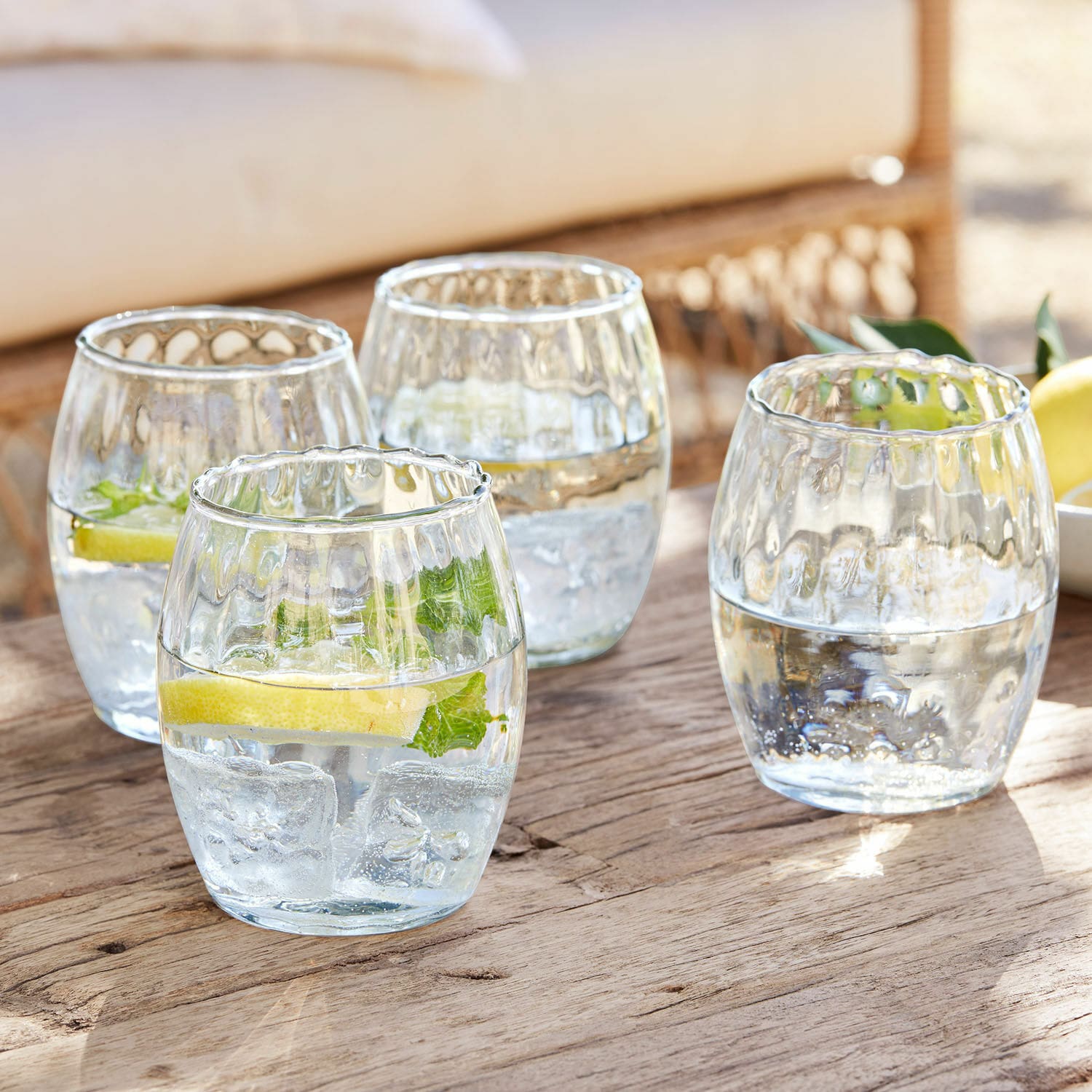 Glas 4er Set Bourgavin Vier Gläser aus klarem Glas mit Wasser, Eis und Zitrone auf einem Holztisch