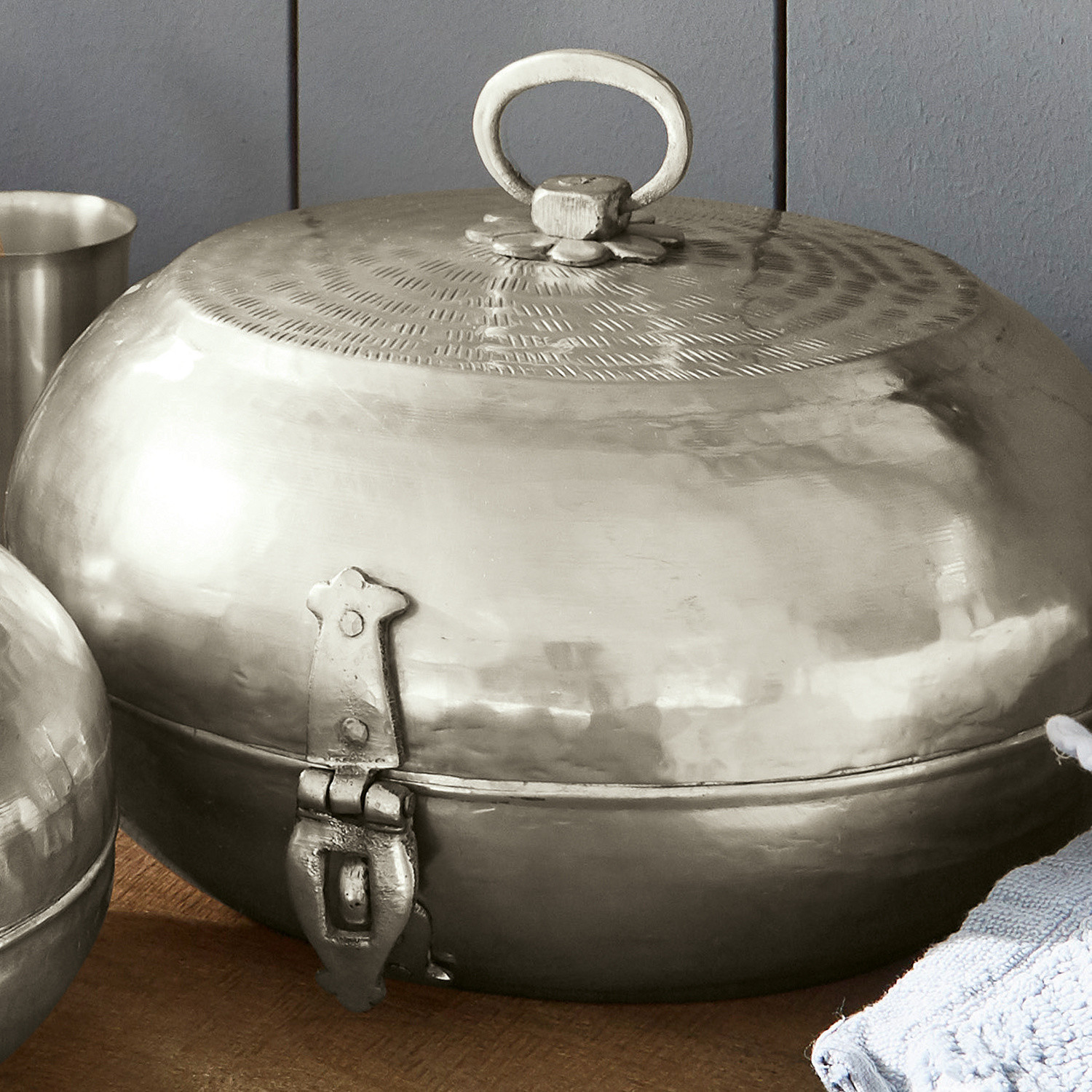 Runder Metallbehälter in Silber mit Deckel und Griff auf Holztisch