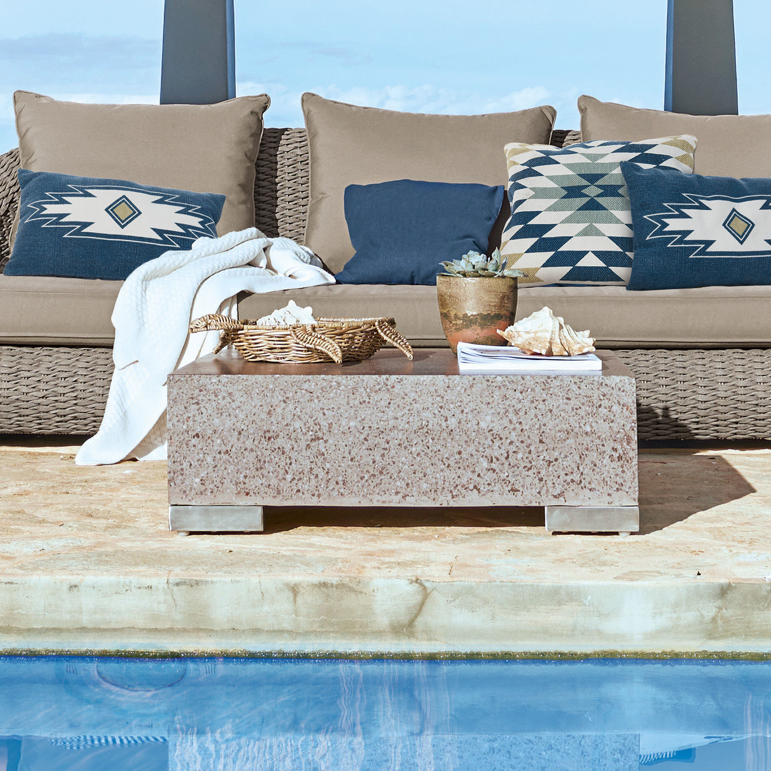Beiger Steintisch auf Terrasse am Pool mit Sofa und dekorativen Kissen im Außenbereich