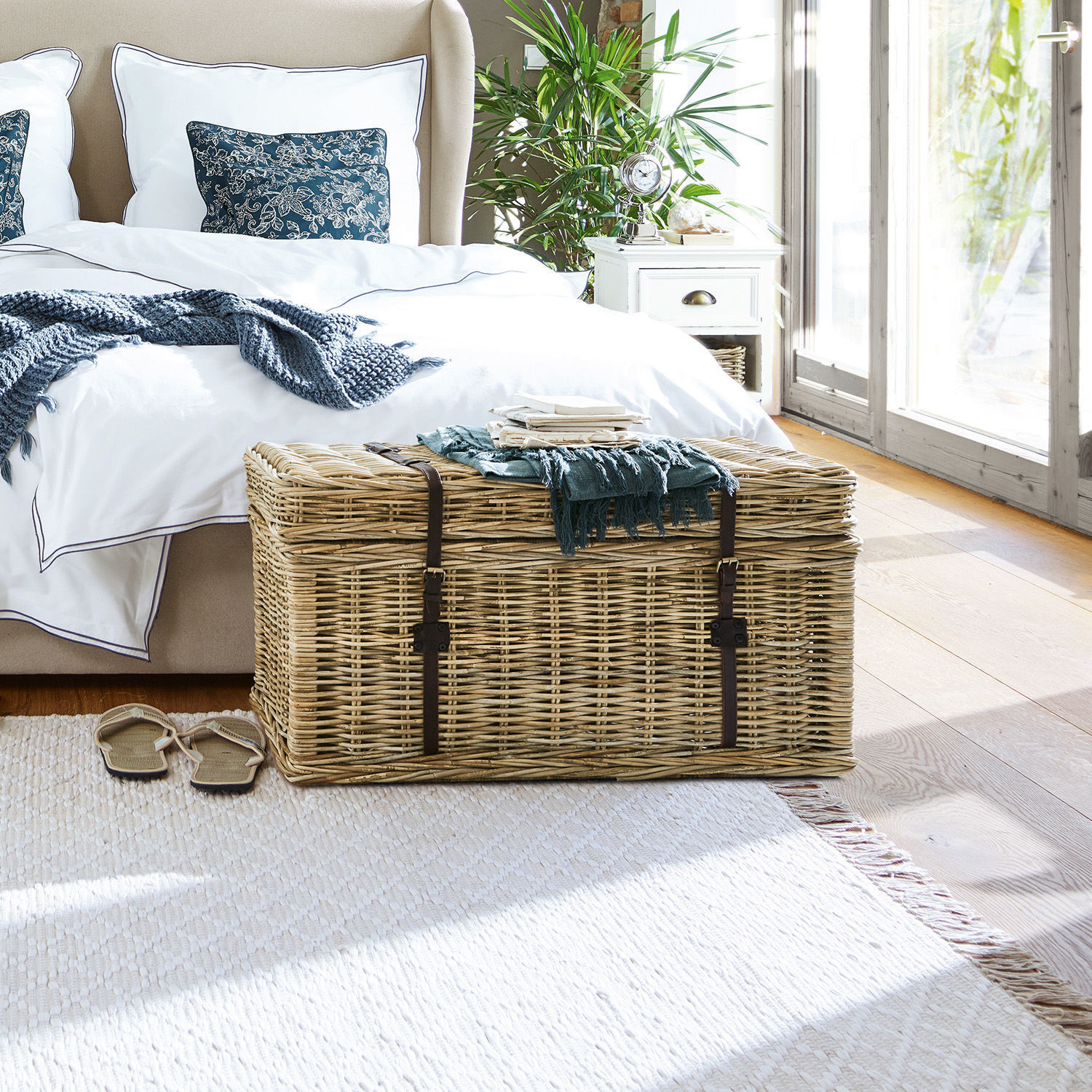 Große naturfarbene Korbtruhe aus Weide mit Lederriemen im hellen Schlafzimmer mit Bett