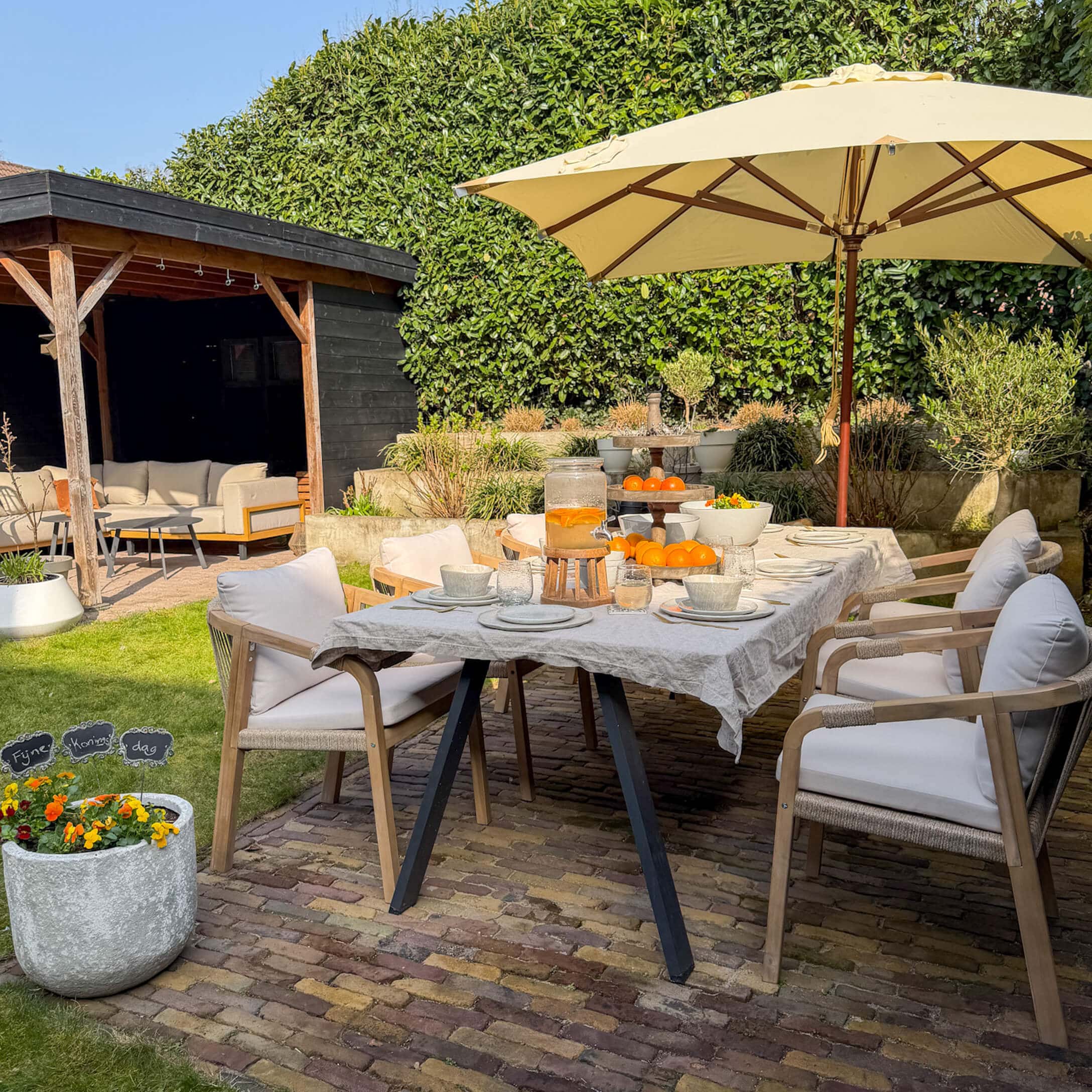 Gartenmöbelset mit Holzstühlen und beigem Sonnenschirm auf gepflasterter Terrasse mit Orangen