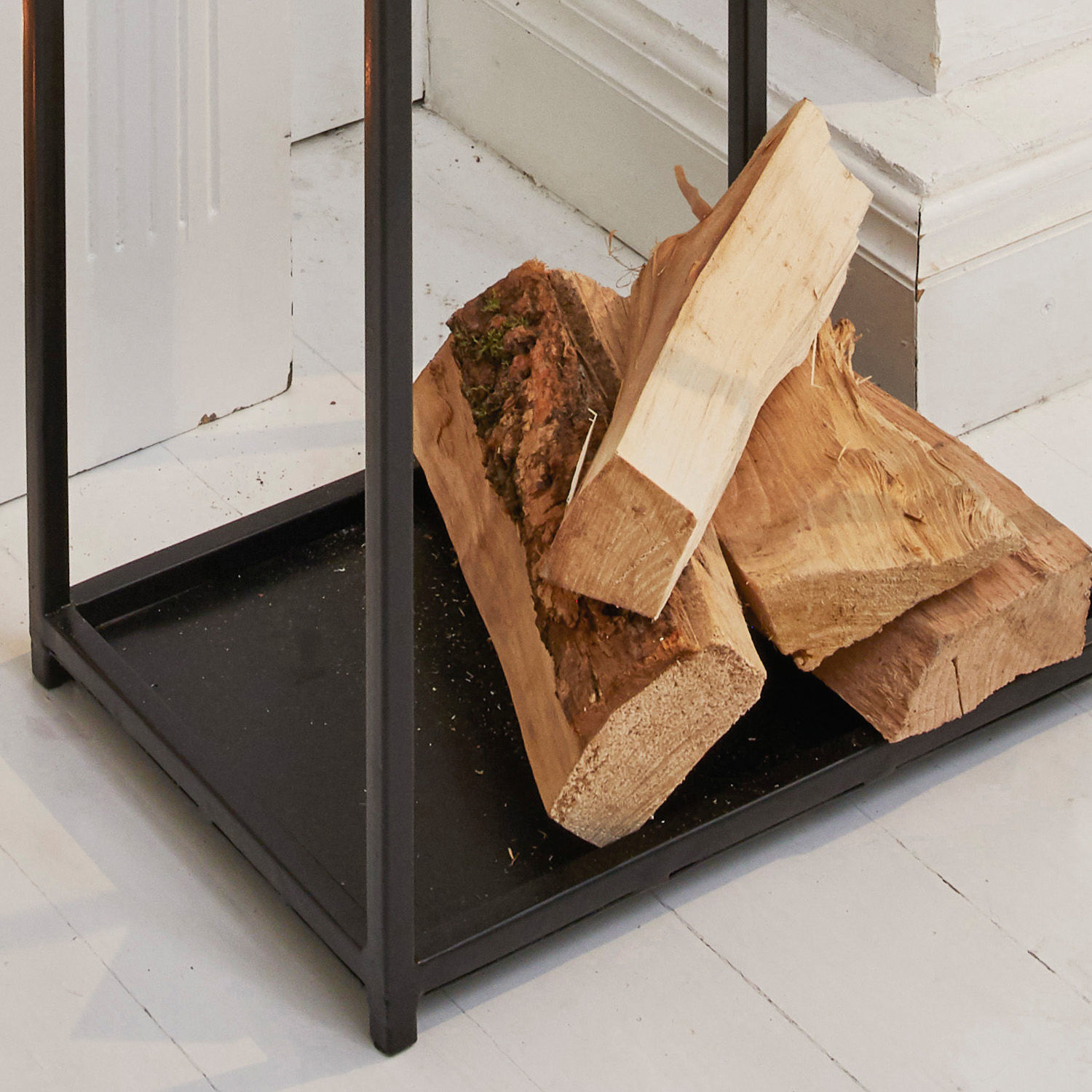Schwarzer Metall-Holzständer mit naturbelassenem Brennholz auf weißem Boden