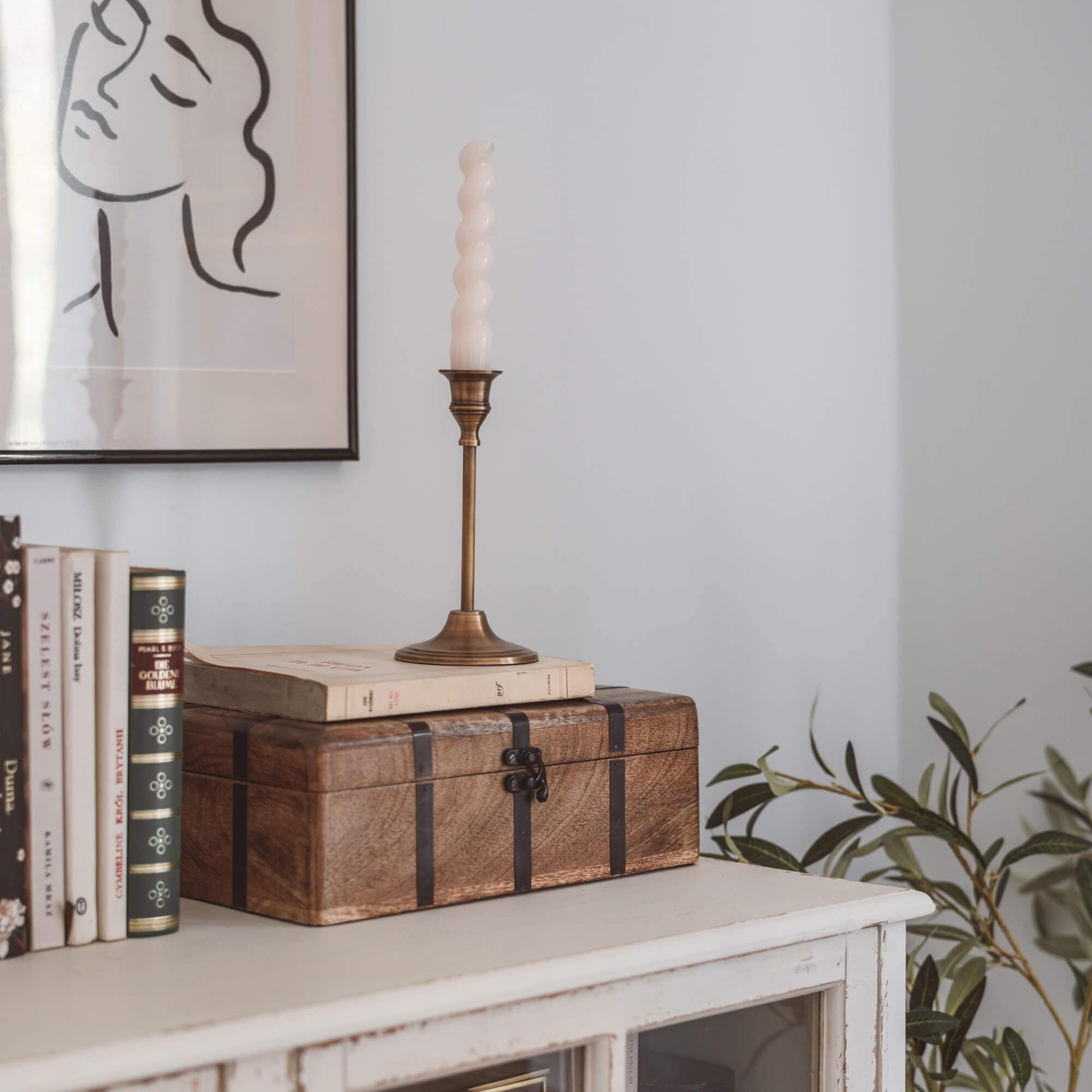 Braune Holzkiste mit Metallbändern auf weißem Sideboard mit Büchern und Kerze