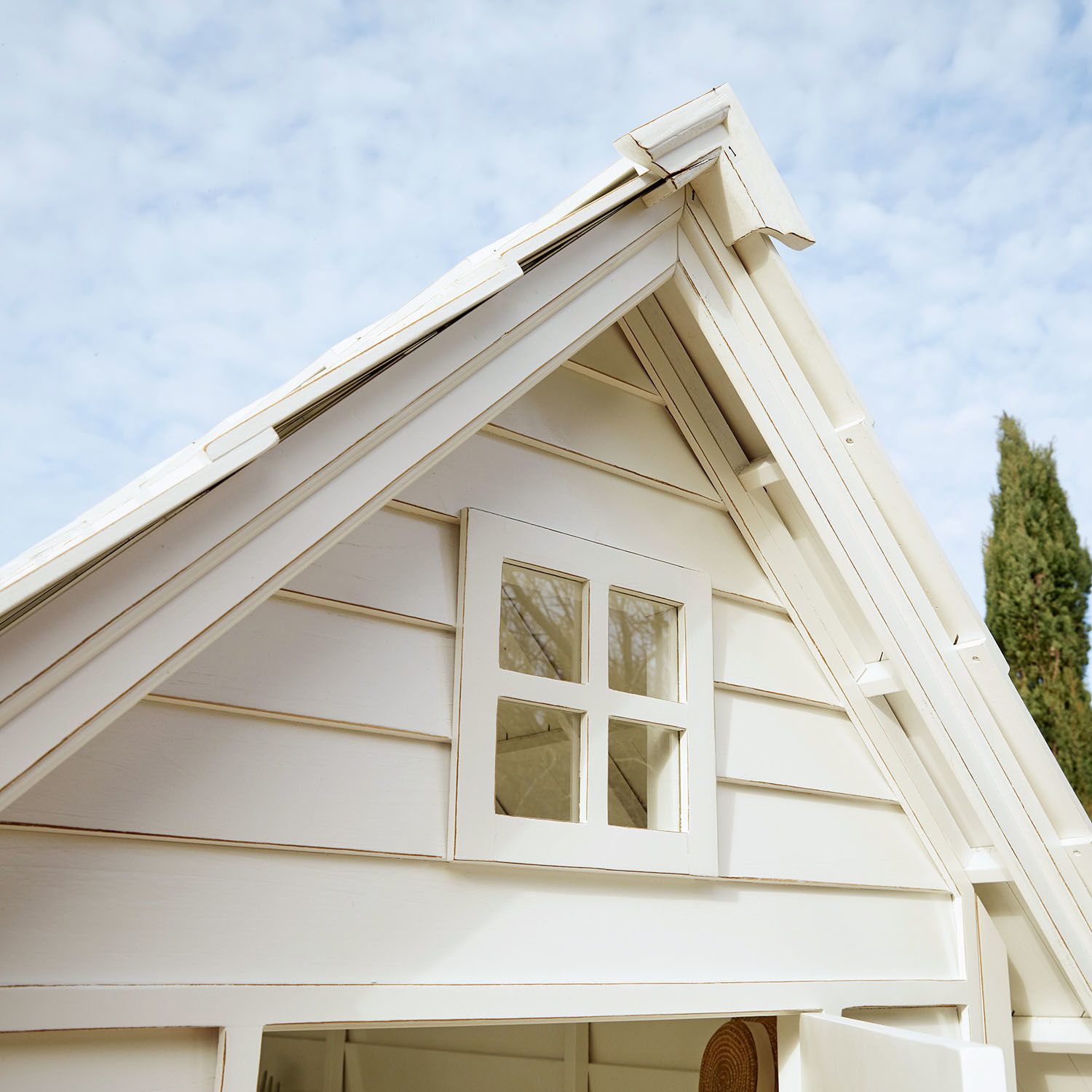Weißes Holzhaus mit kleinem Fenster und schrägem Dach im Garten