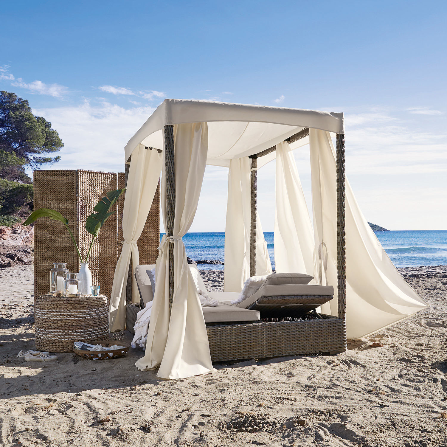 Rattan-Liegestuhl mit cremefarbenen Vorhängen am Strand, Outdoor-Möbel für entspannte Stunden