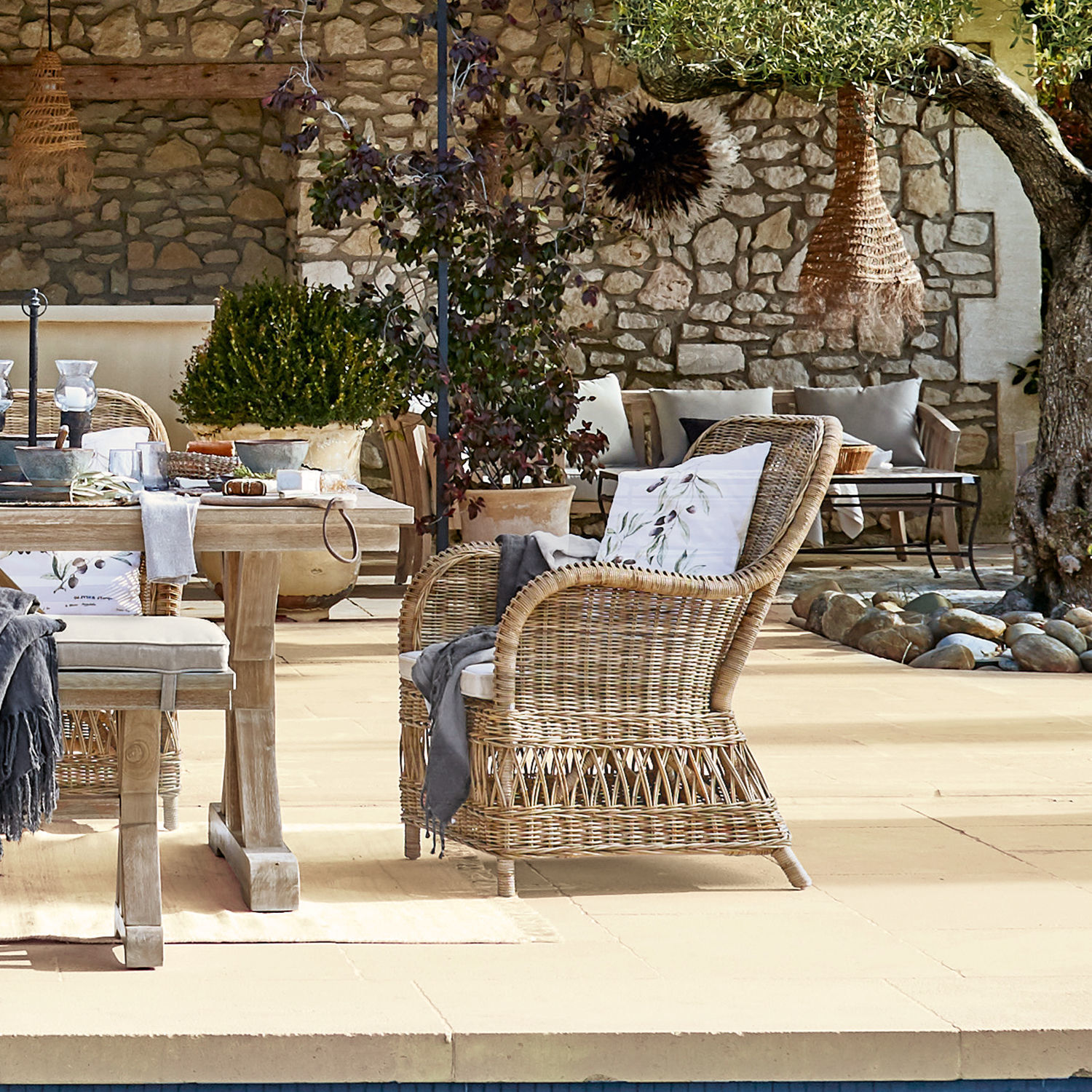 Natürlicher Rattansessel in Beige auf Terrasse mit Steinmauer und rustikalem Holztisch