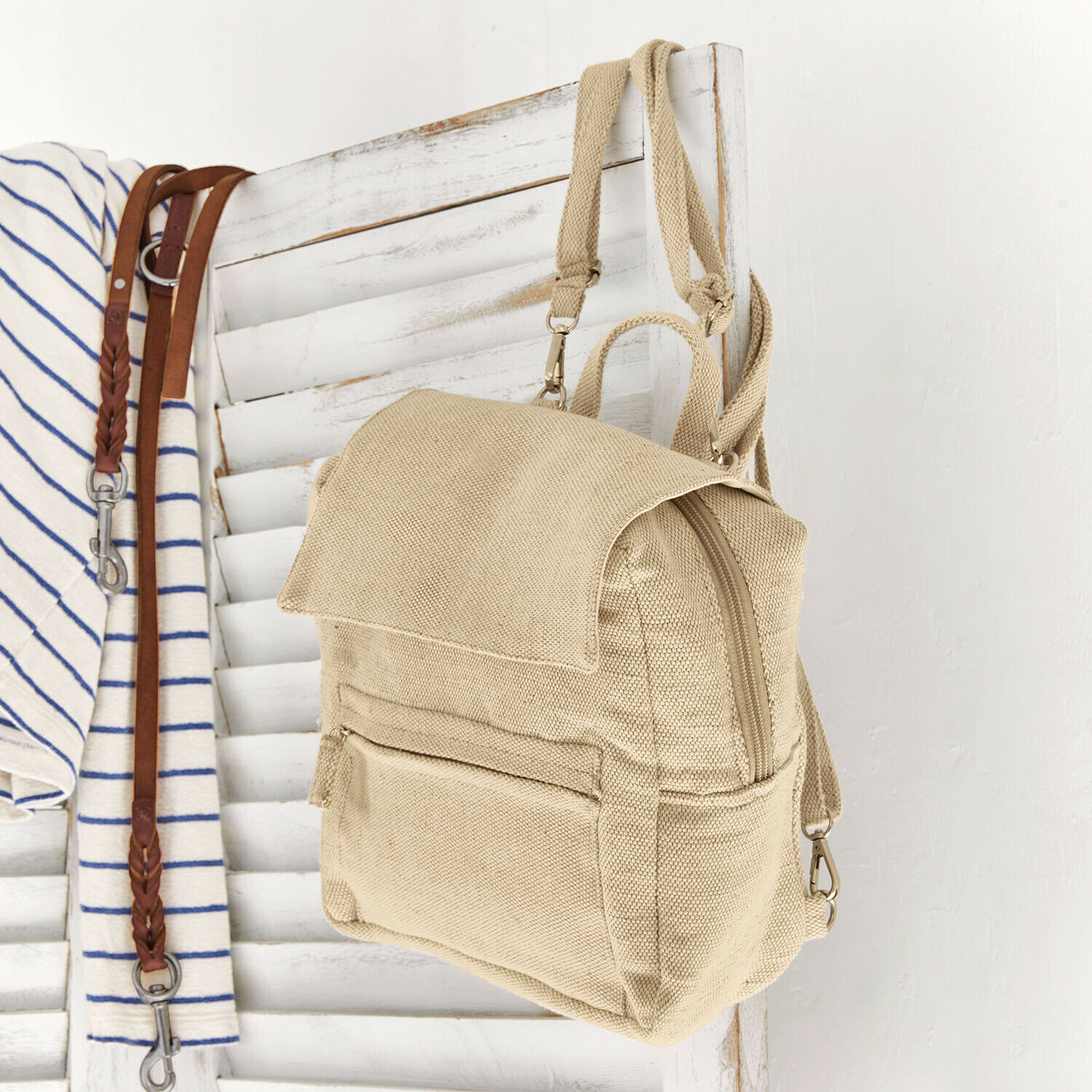 Beiger Rucksack aus Stoff an weißem Holzgitter hängend, praktisch und leicht für den Alltag