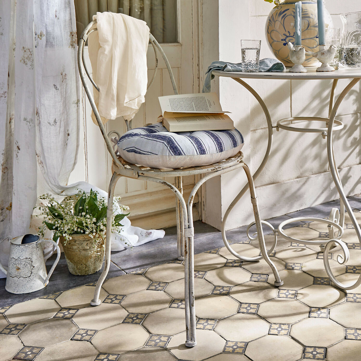 Stuhl Aube Vintage Metallstuhl mit blau-weiß gestreiftem Kissen und weißem Tuch im hellen Raum mit Fliesenboden