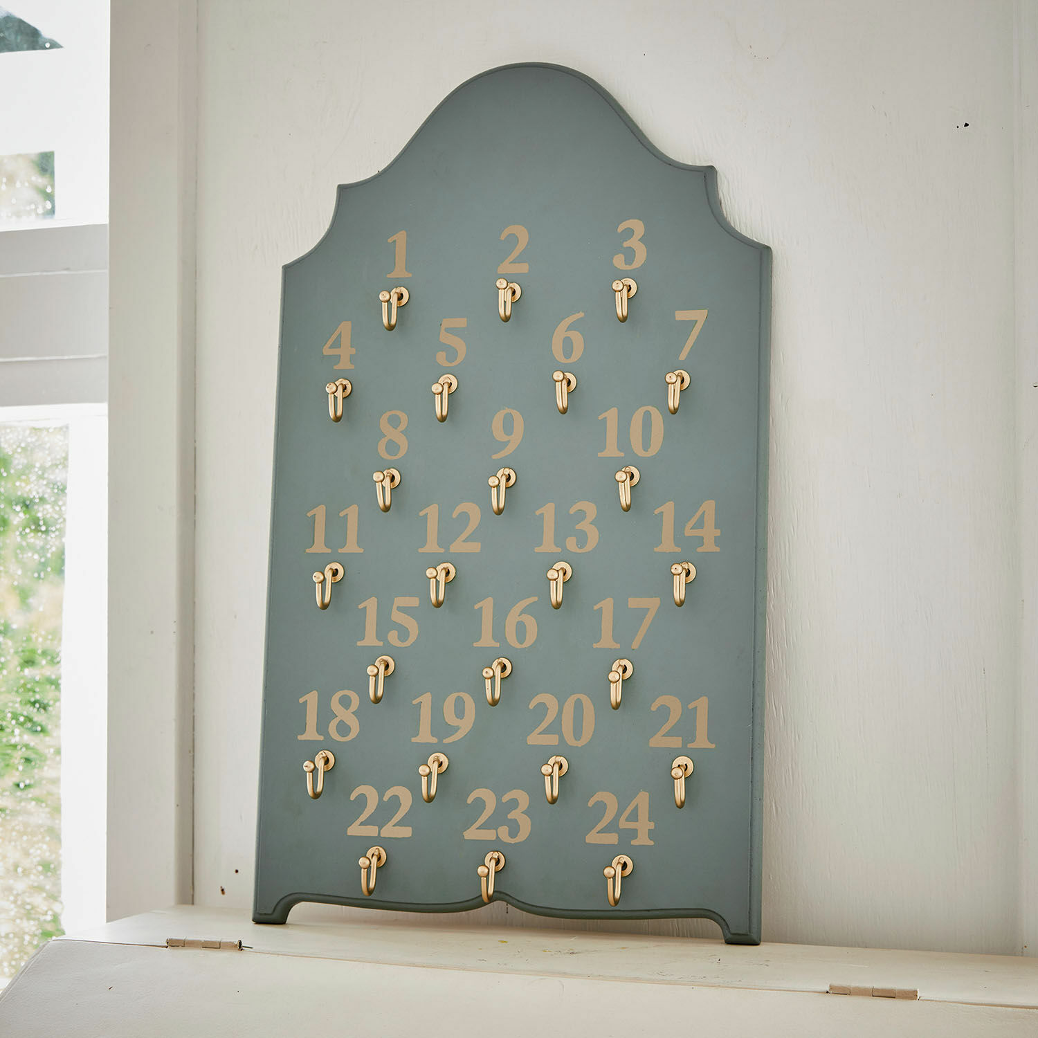 Blaues Holzbrett mit 24 goldenen Haken und Zahlen für Adventskalender