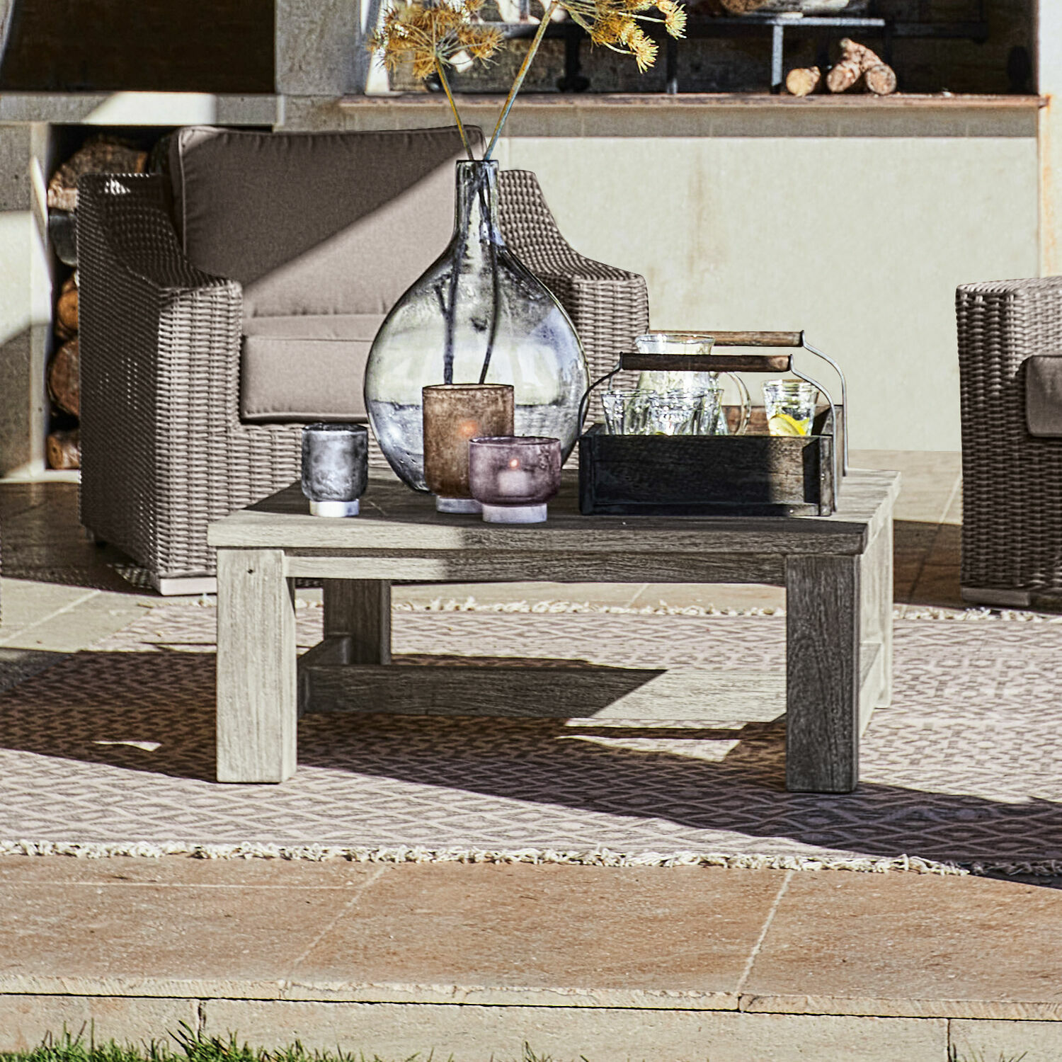Couchtisch Malden Niedriger Holztisch auf Terrasse mit dekorativen Kerzen und Vase, Rattan-Gartenmöbel im Hintergrund