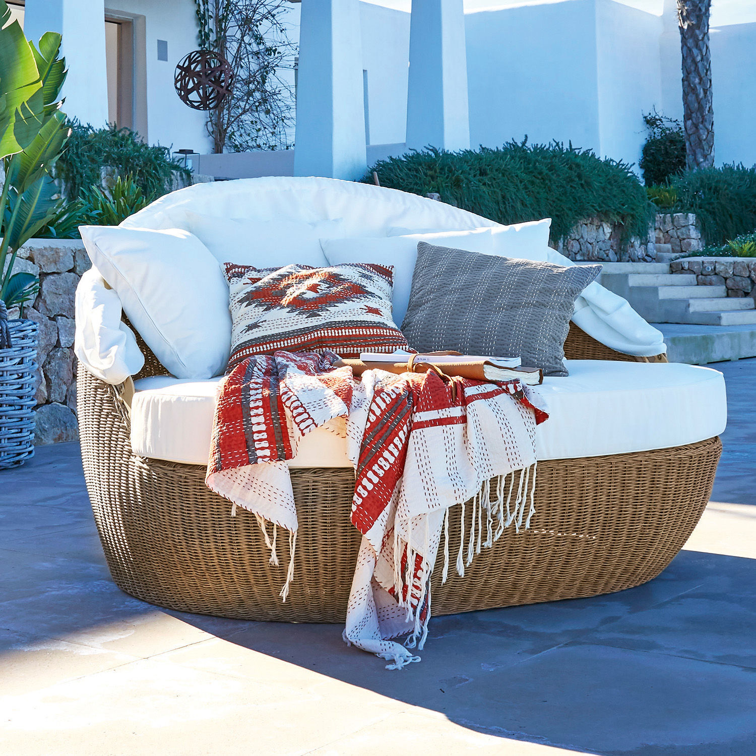 Runder Rattansessel mit weißem Kissen und rot-weißem Plaid für Terrasse oder Garten