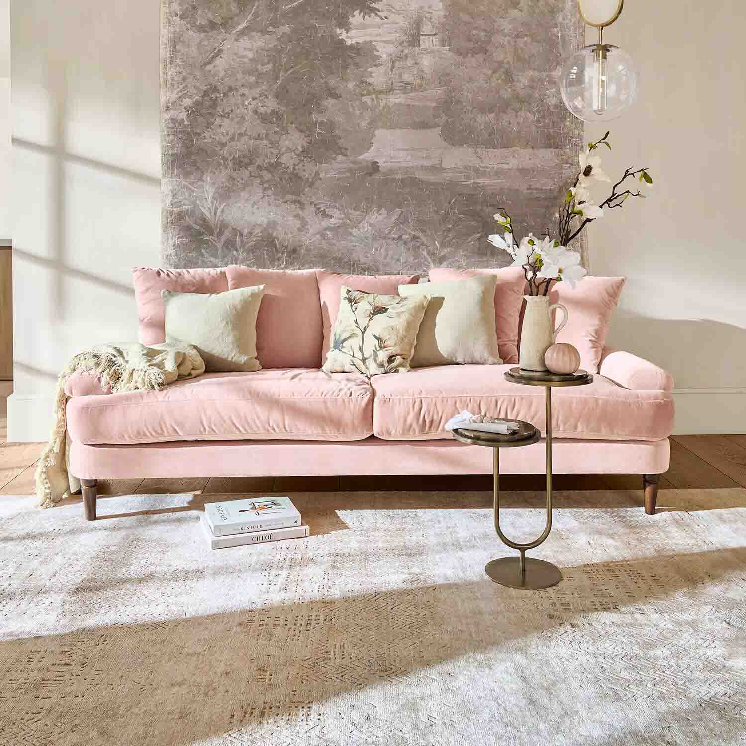 Rosa Samtsofa mit Kissen und Beistelltisch in hellem Wohnzimmer mit Wanddekoration