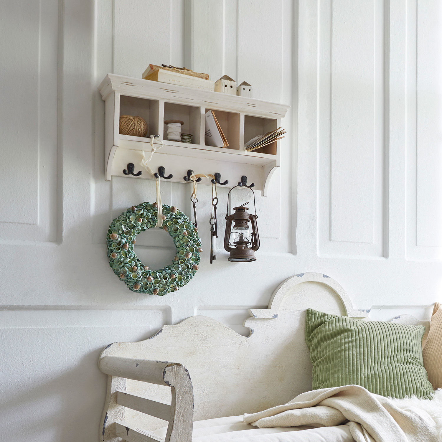 Weißes Holz-Wandregal mit Haken, Vintage-Deko und grünem Kranz an der Wand im Landhausstil