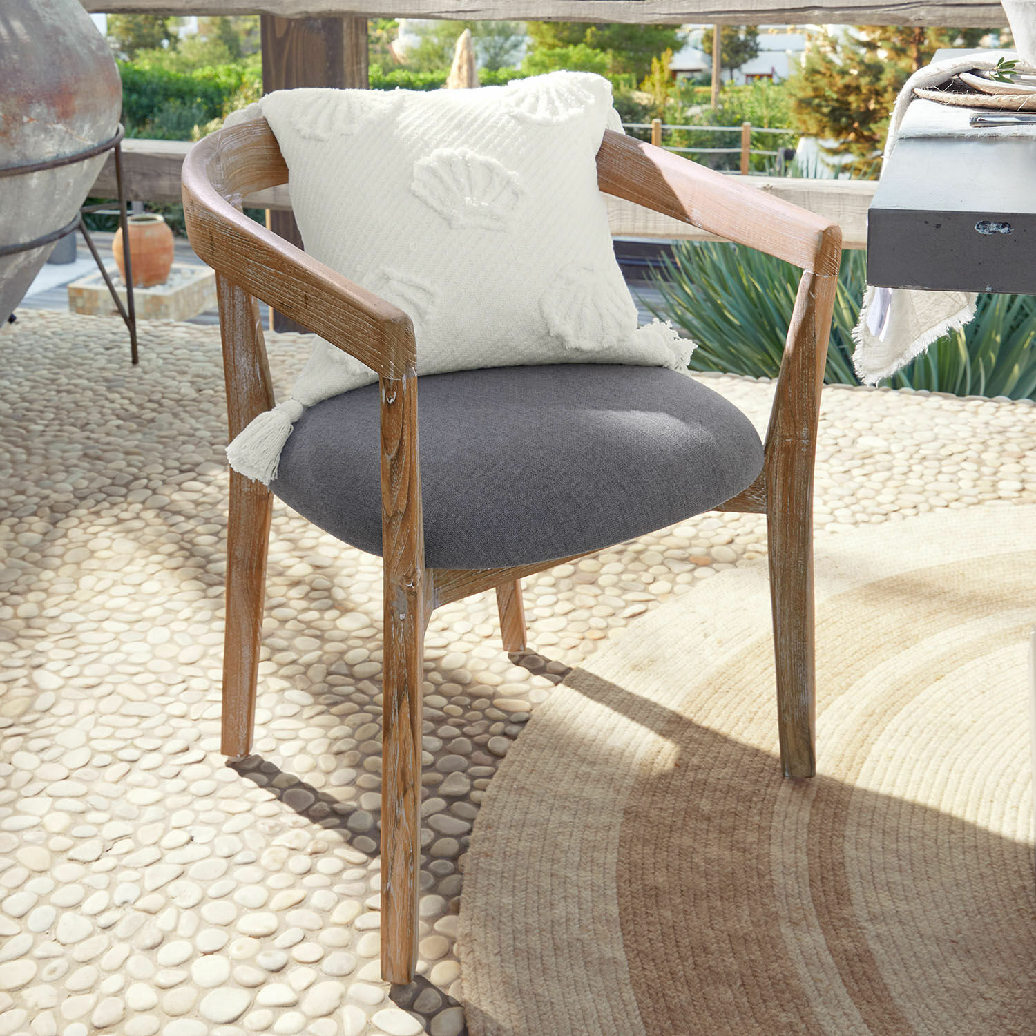 Stuhl Lunebois Stuhl aus Holz mit grauem Polstersitz und weißem Dekokissen auf sonniger Terrasse