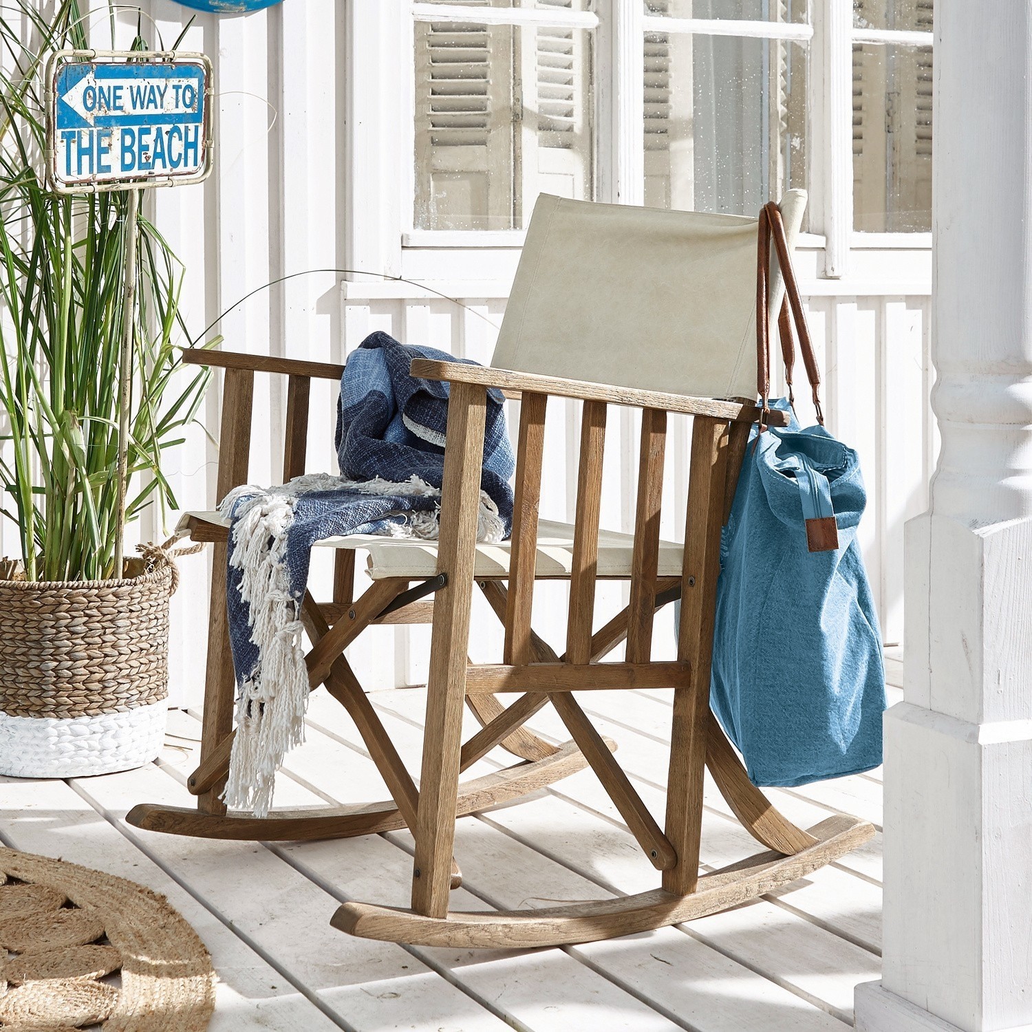 Holzschaukelstuhl mit beigem Stoff, blauem Decken und Tasche auf heller Terrasse im Strandstil