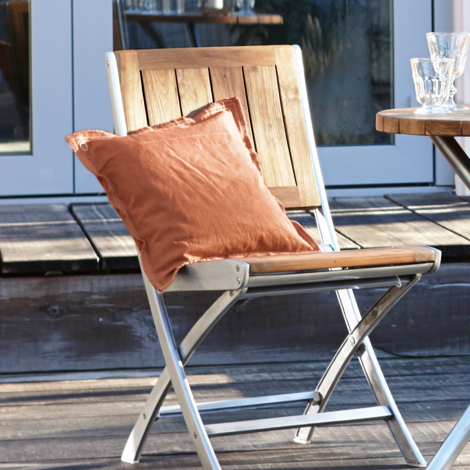 Klappstuhl aus Holz und Metall mit orangefarbenem Kissen auf sonniger Terrasse