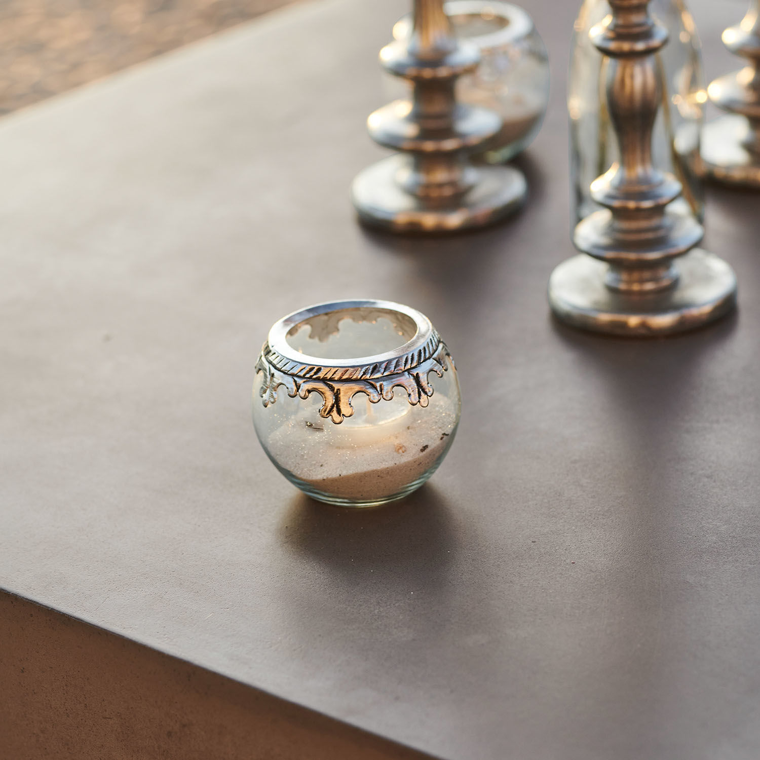 Glas-Teelichthalter mit silbernem Metallornament auf Sand, elegante Tischdekoration