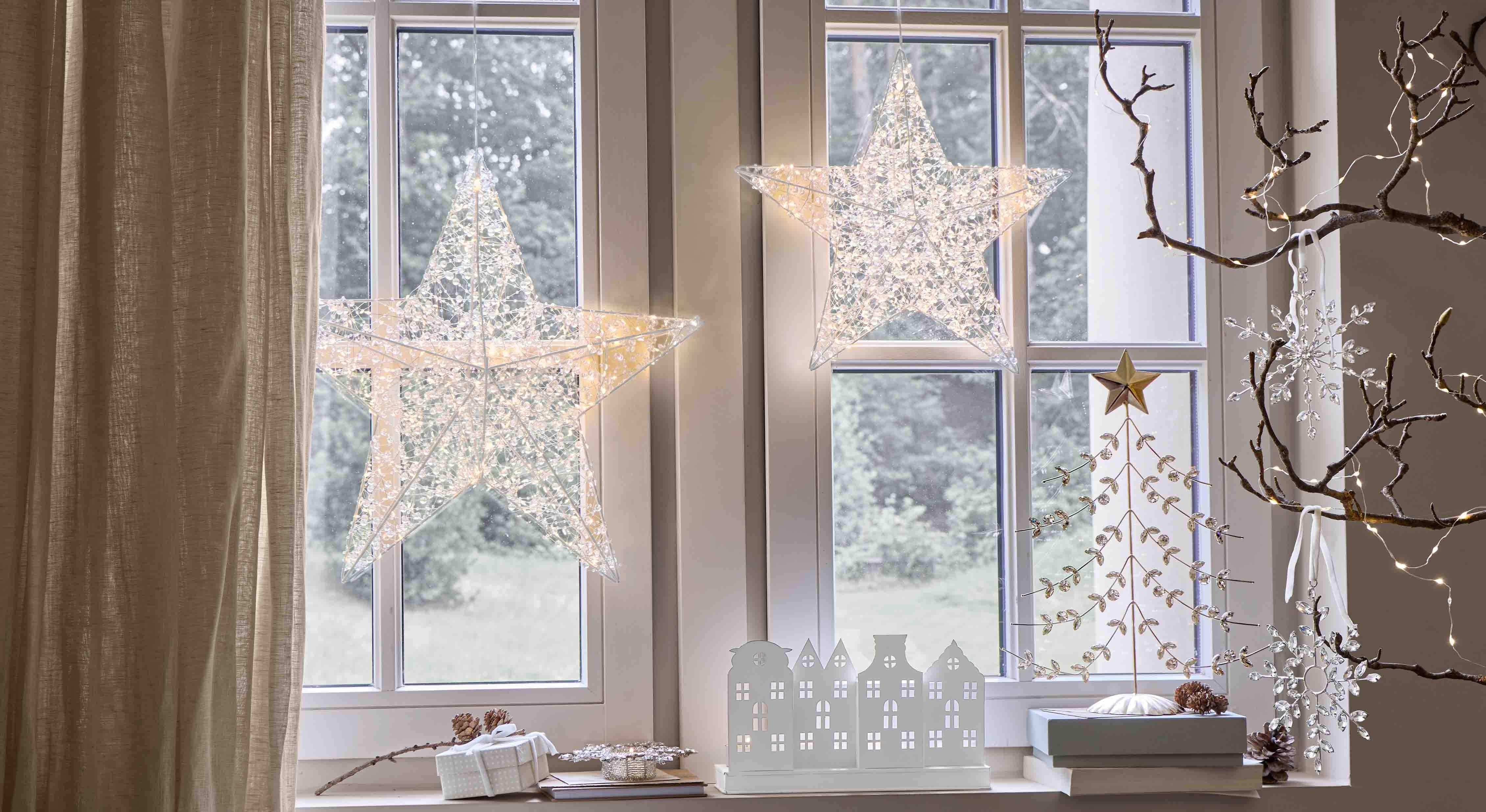 Dekorative Leuchtsterne aus transparentem Material am Fenster hängend, festliche Innenbeleuchtung