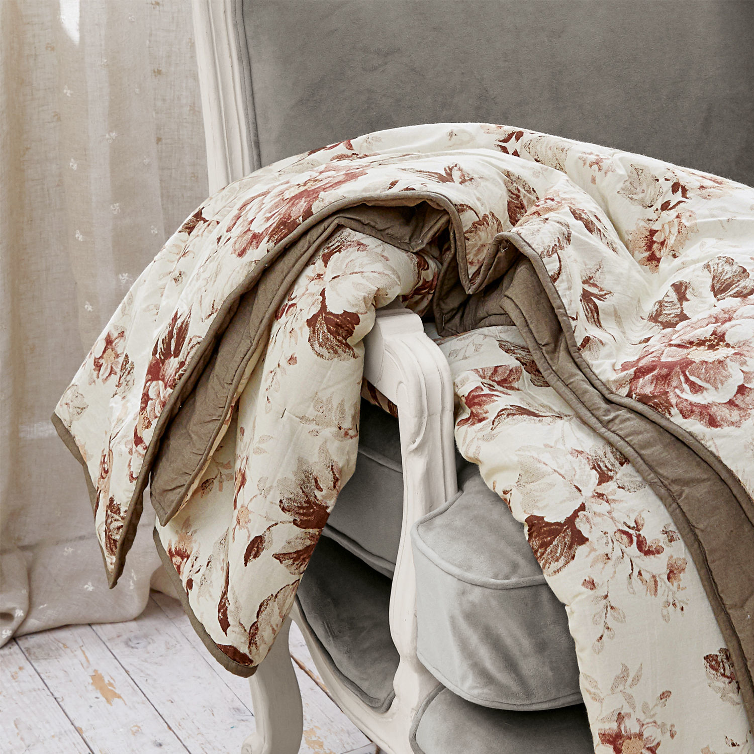 Baumwoll-Decke in Creme mit braunen Blumen auf grauem Sessel, dekorativer und weicher Wohntextil