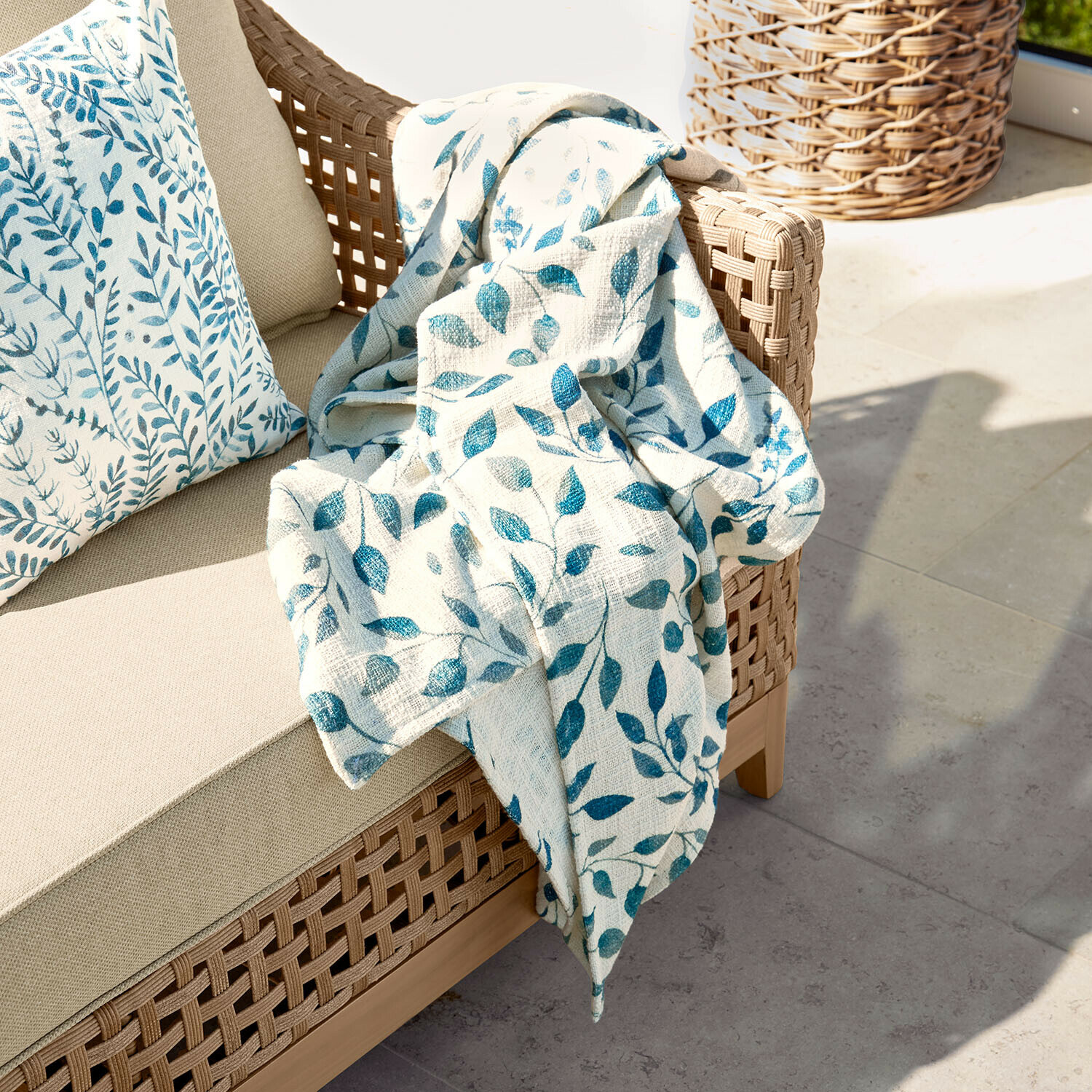 Beiges Sofa mit geflochtenem Rücken und cremefarbiger Decke mit blauem Blattmuster auf Terrasse