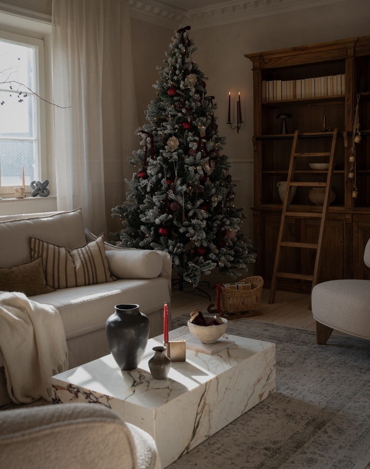 Gemütliches Wohnzimmer mit künstlichem Weihnachtsbaum in Grün-Rot und einem Marmortisch als Couchtisch