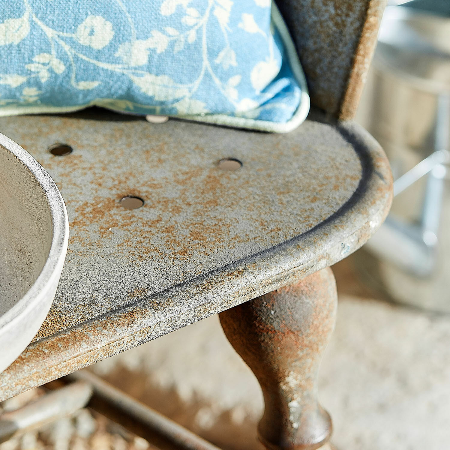 Nahaufnahme eines rostigen Metallstuhlsitzes mit blauem Kissen und runden Lüftungslöchern