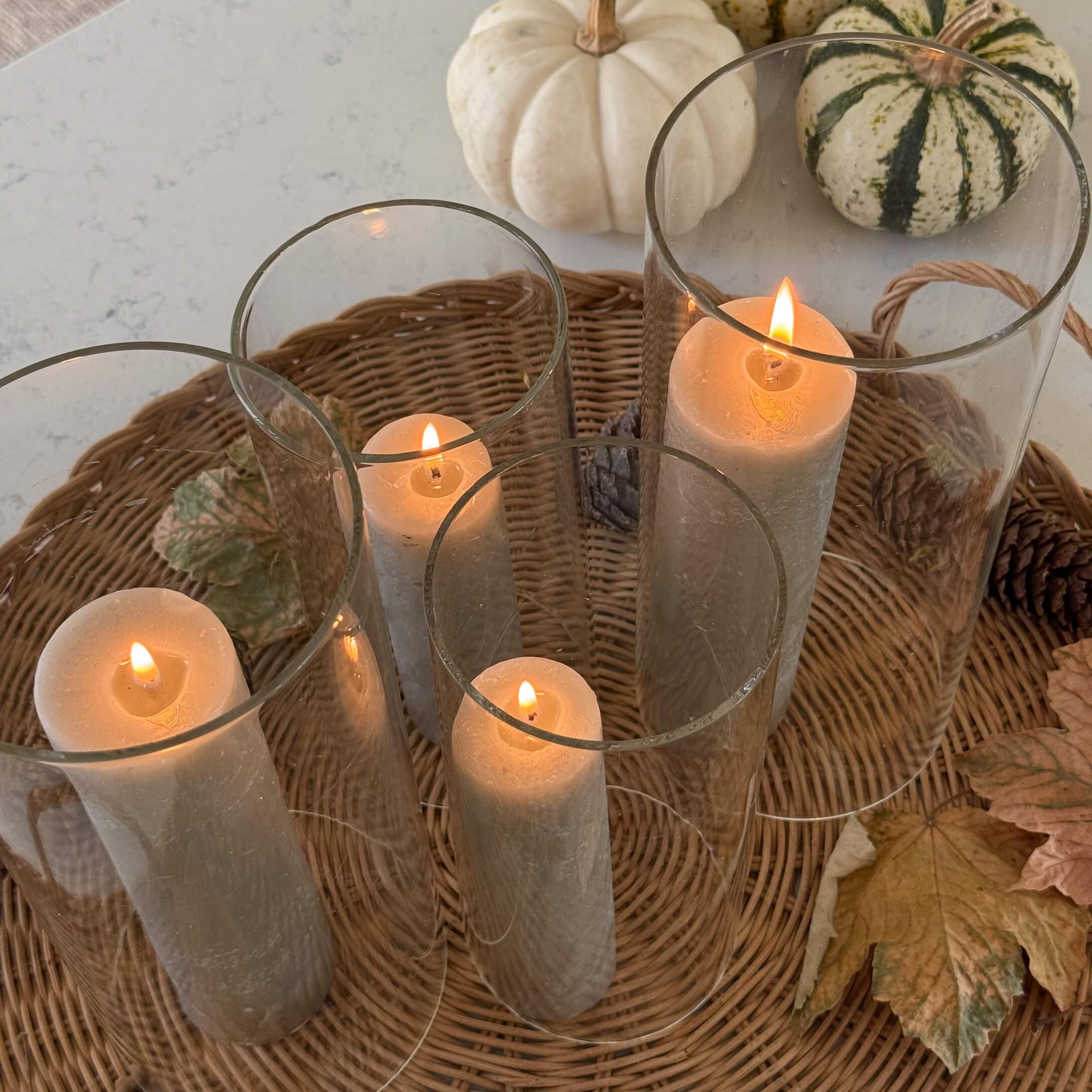 Vier Glaswindlichter mit beigen Kerzen auf einem Korbtablett mit herbstlicher Dekoration