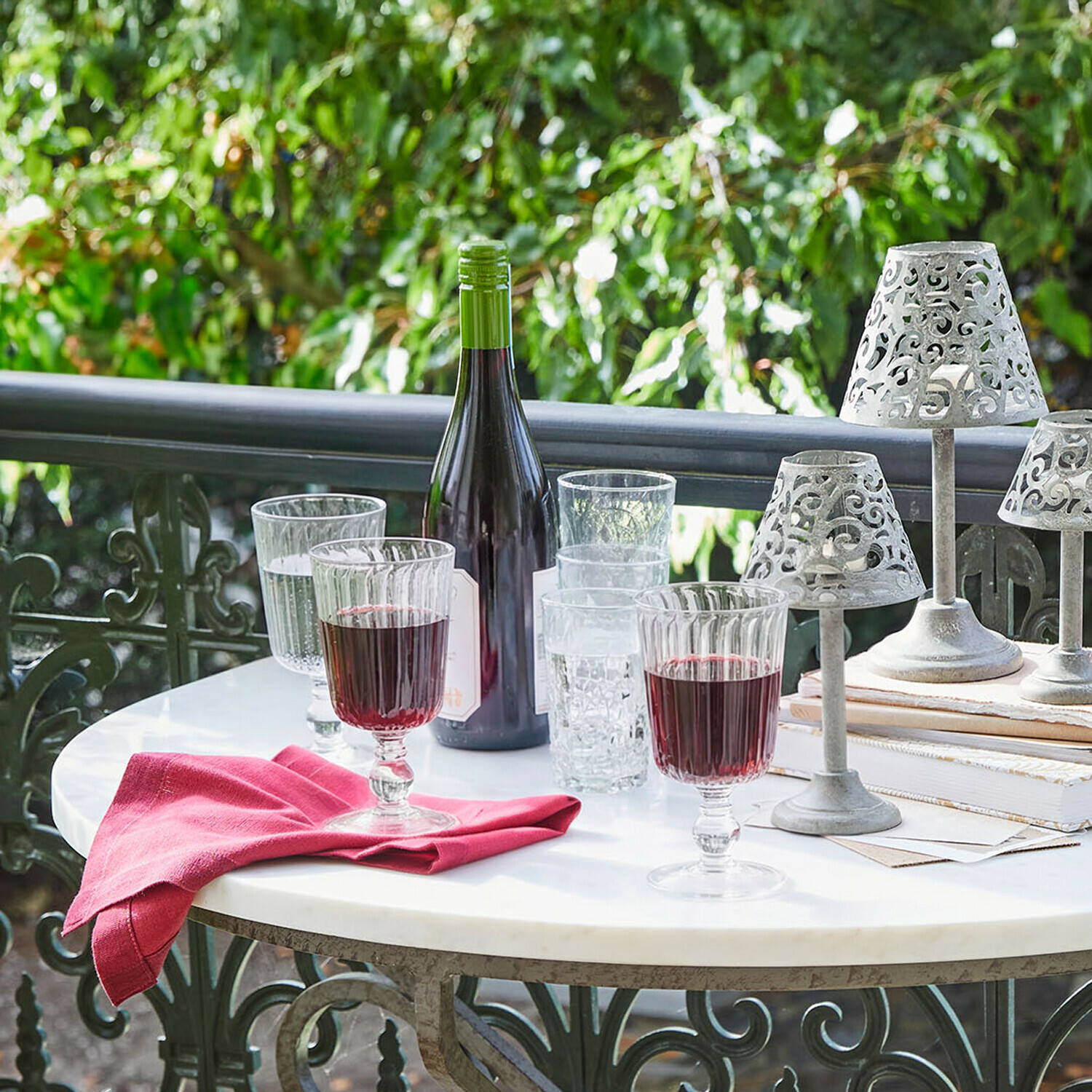 Gläser mit Rotwein und Flasche auf weißem Tisch mit dekorativen Metalllampen im Garten