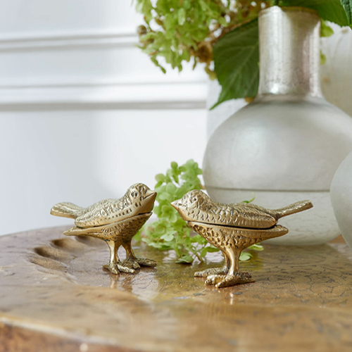 Zwei dekorative Vogel-Figuren aus goldenem Metall auf einem Holztisch als Wohnaccessoire