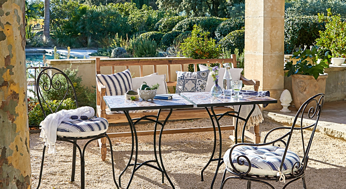 Gartenmöbel-Set mit Metallstühlen und Holzbank auf Terrasse mit gestreiften Kissen und Tisch mit Fliesen