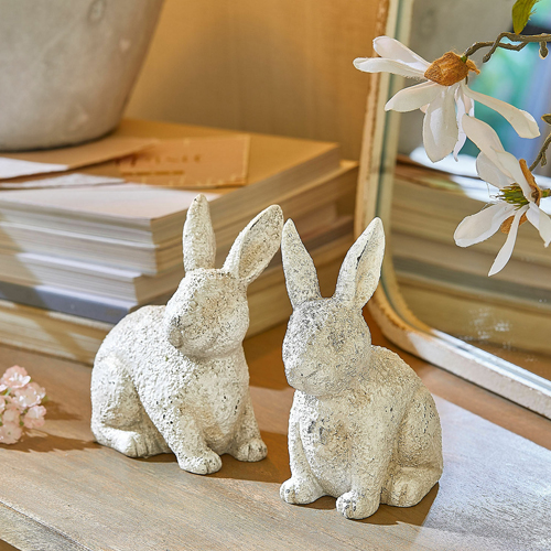 Zwei weiße Hasenfiguren aus strukturiertem Material auf Holztisch, frühlingshafte Dekoration